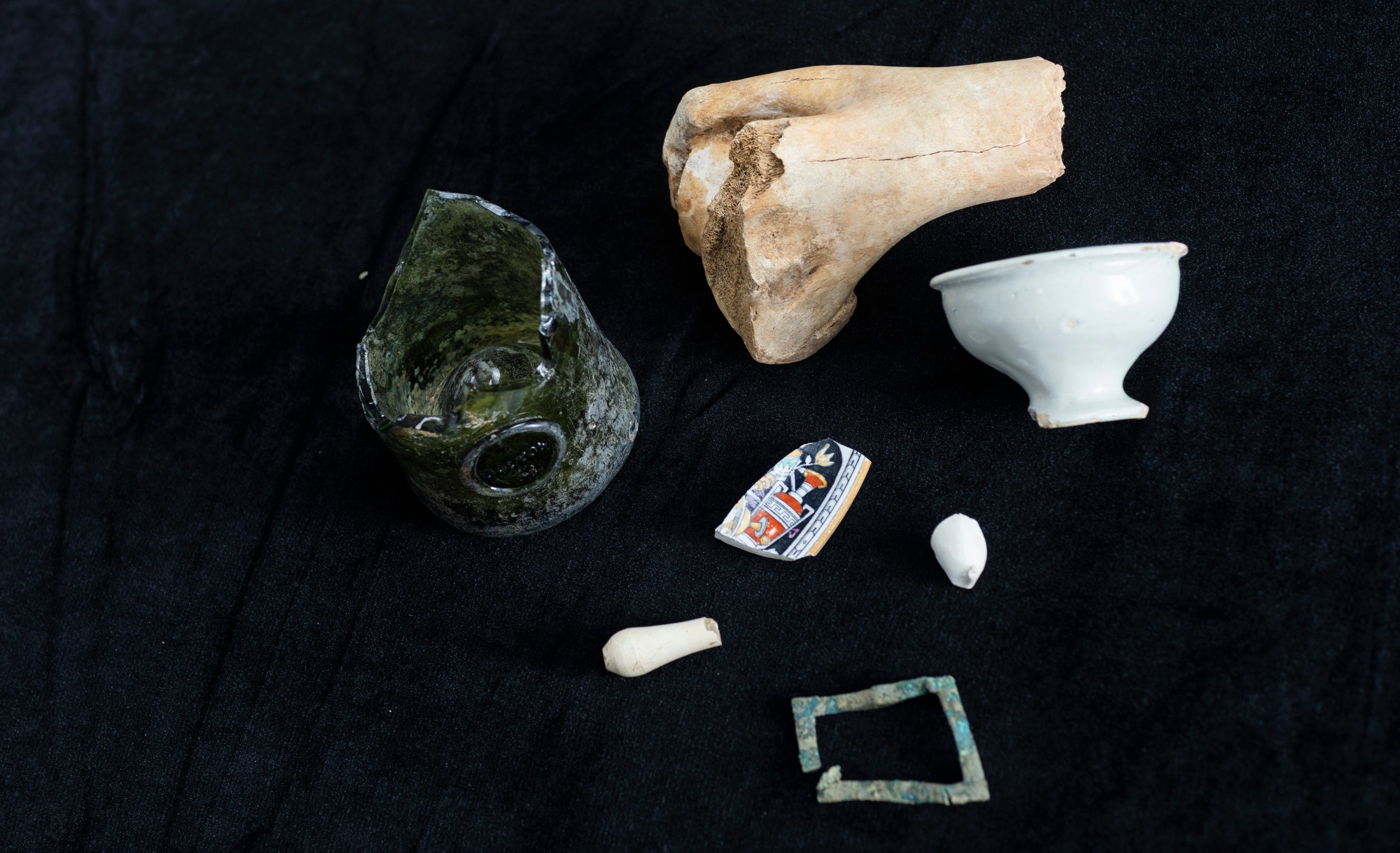 Each of the discoveries set on a black background, includes fragments of a bone, wine bottle, ointment pot, buckle, glazed plate, wig curler and clay pipe