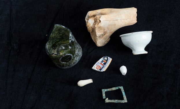 Each of the discoveries set on a black background, includes fragments of a bone, wine bottle, ointment pot, buckle, glazed plate, wig curler and clay pipe