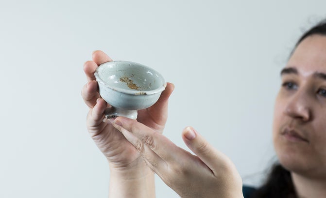 A person appears fuzzy in the background holding a near complete Georgian ointment pot which is a white clay bowl.