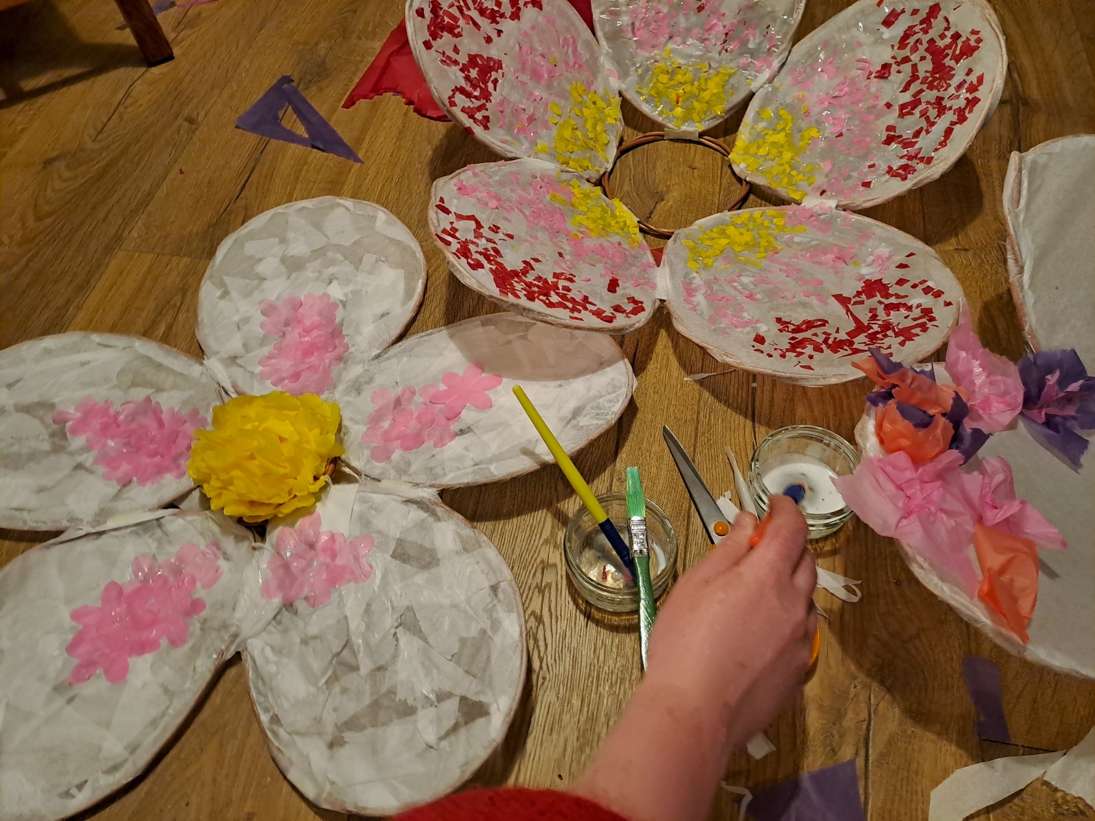 A selection of in-progress blossom lanterns on the floor, with a hand adding decorations.