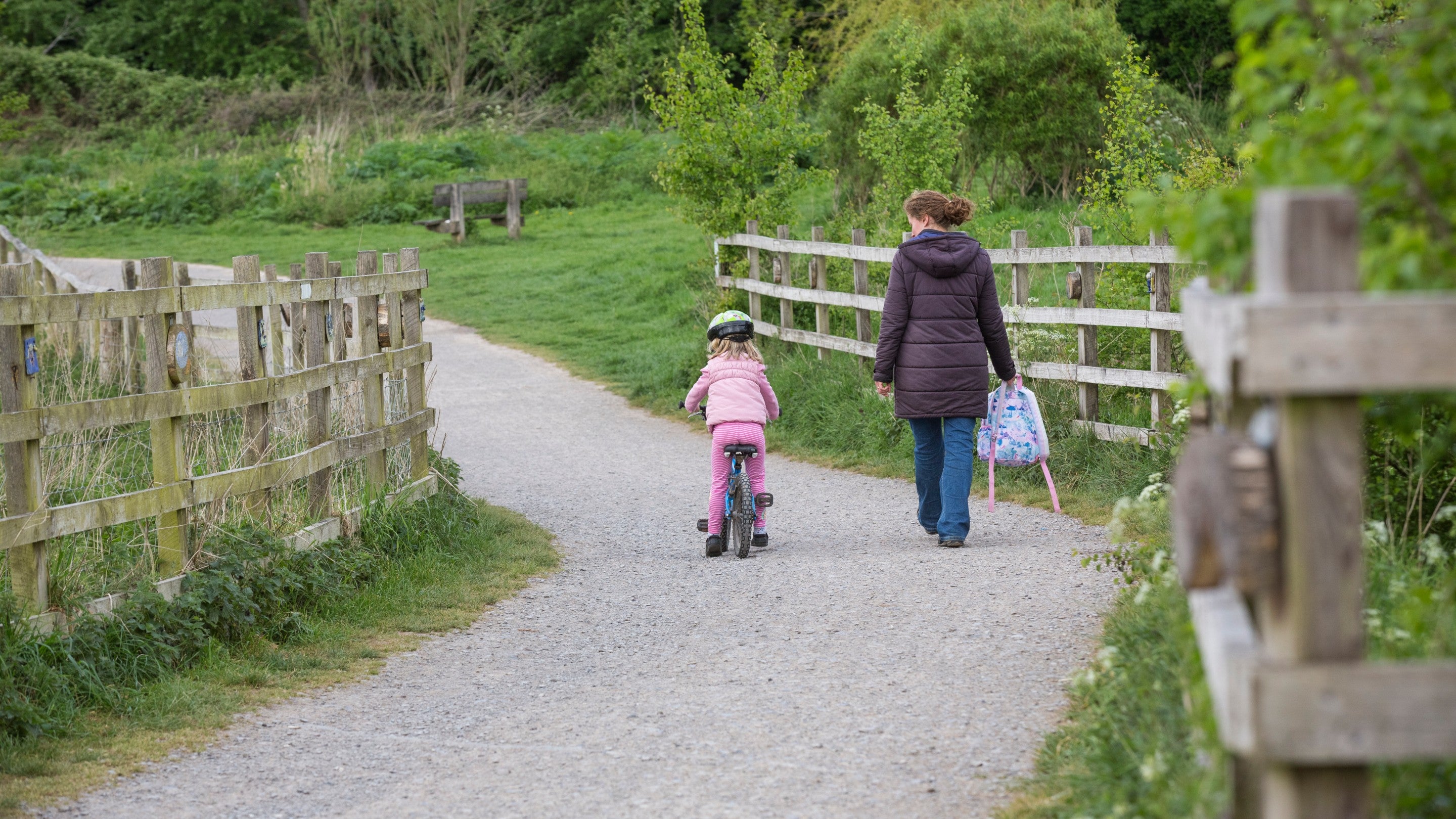 A visitor walking and their child riding a bike along the path towards the meadows.