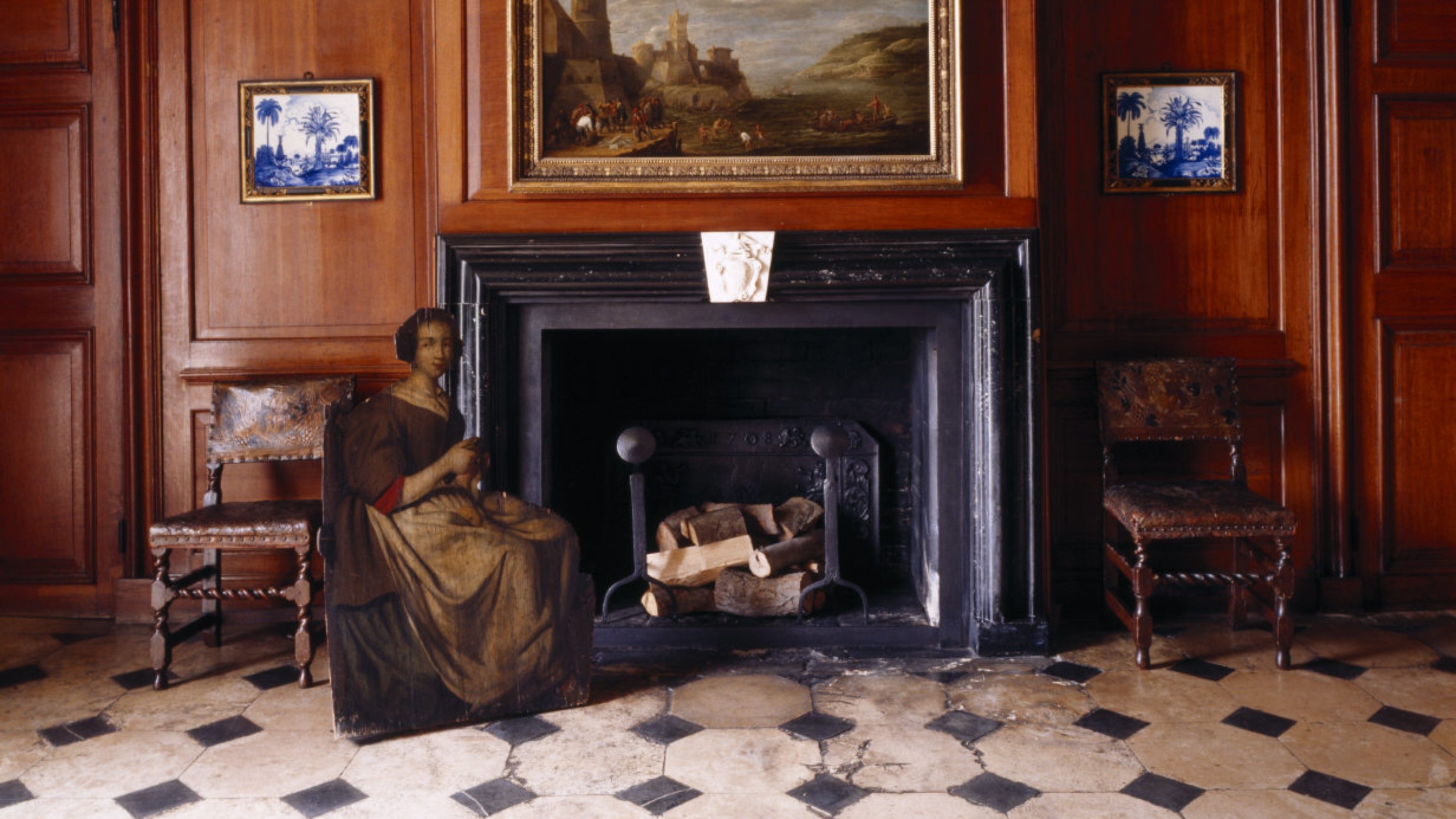 A view of the fireplace in the West Hall at Dyrham Park, with a dummy-board figure of a woman peeling an apple sits beside the fireplace