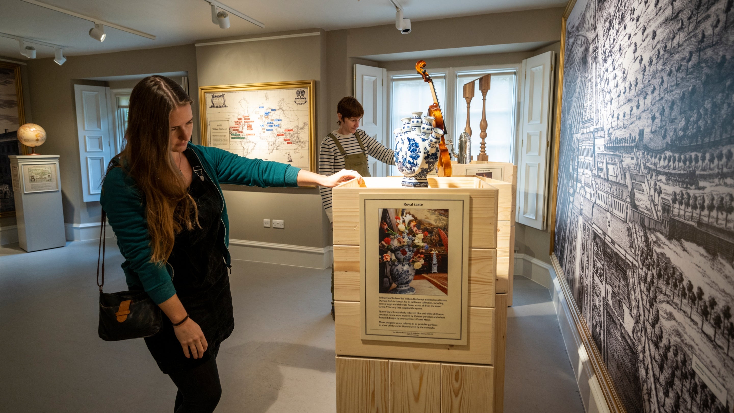 Two women look at a display of information stands in a room at Dyrham Park, South Gloucestershire
