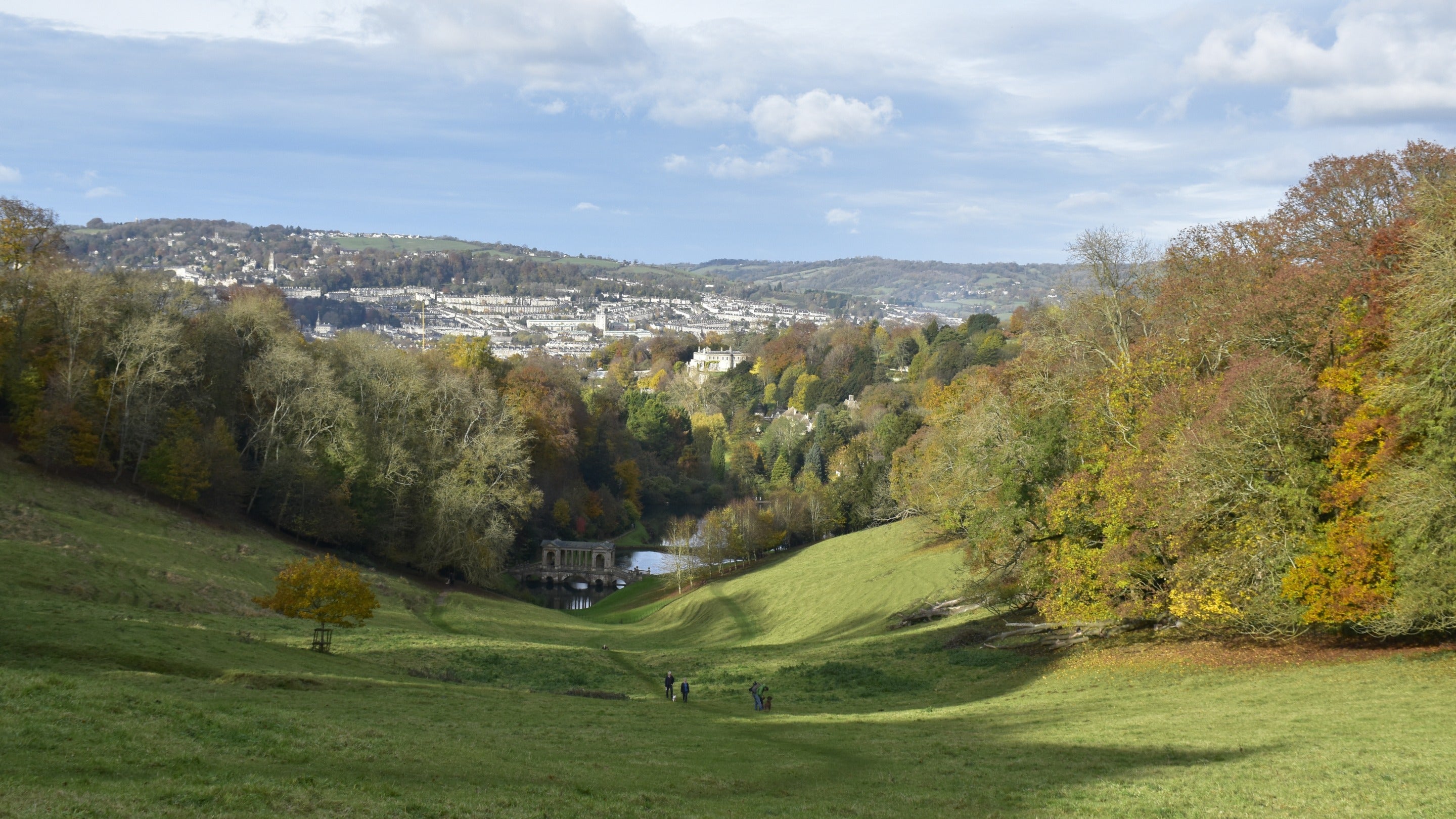 View of the landscape in autumn at Prior Park with people walking and the city of Bath in the distance.