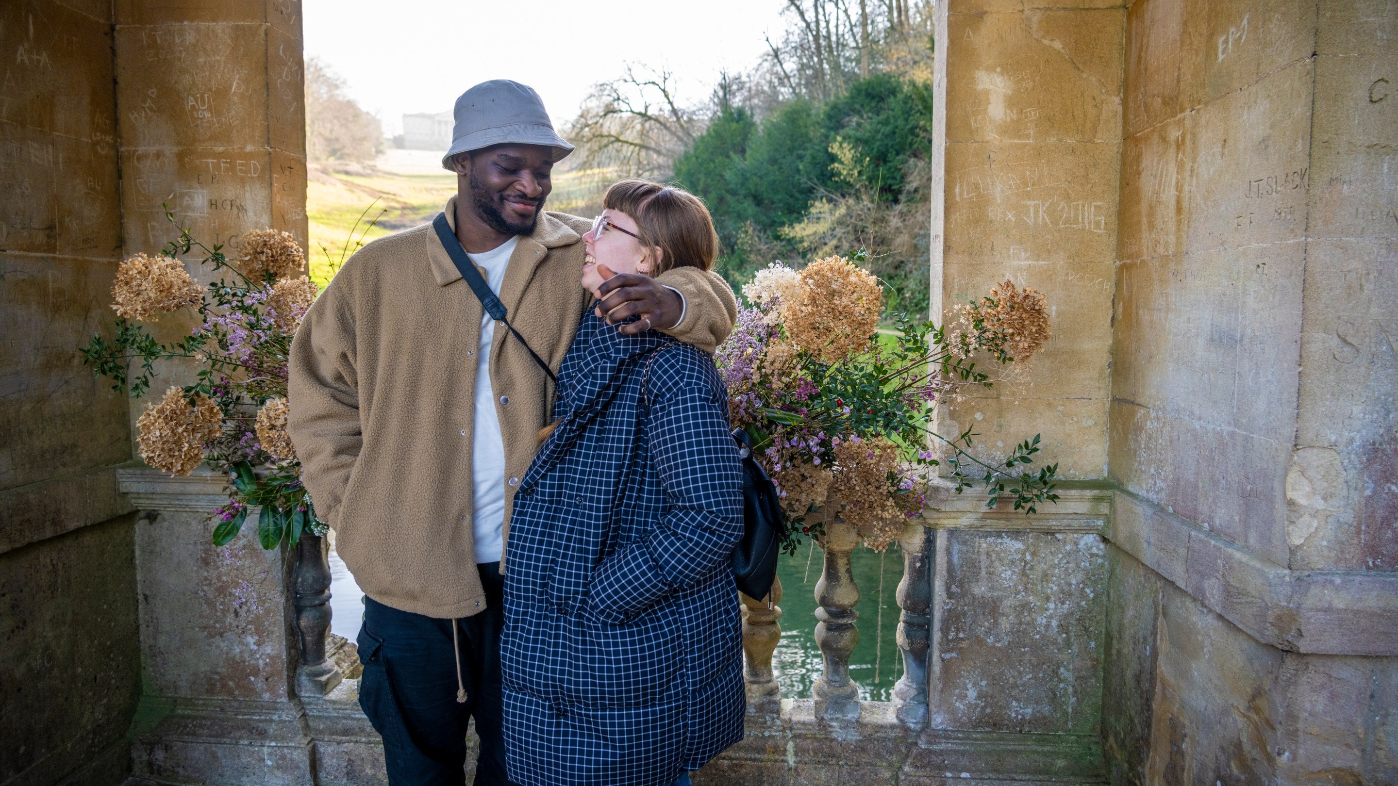A couple on the bridge at Prior Park with dried flowers behind them.