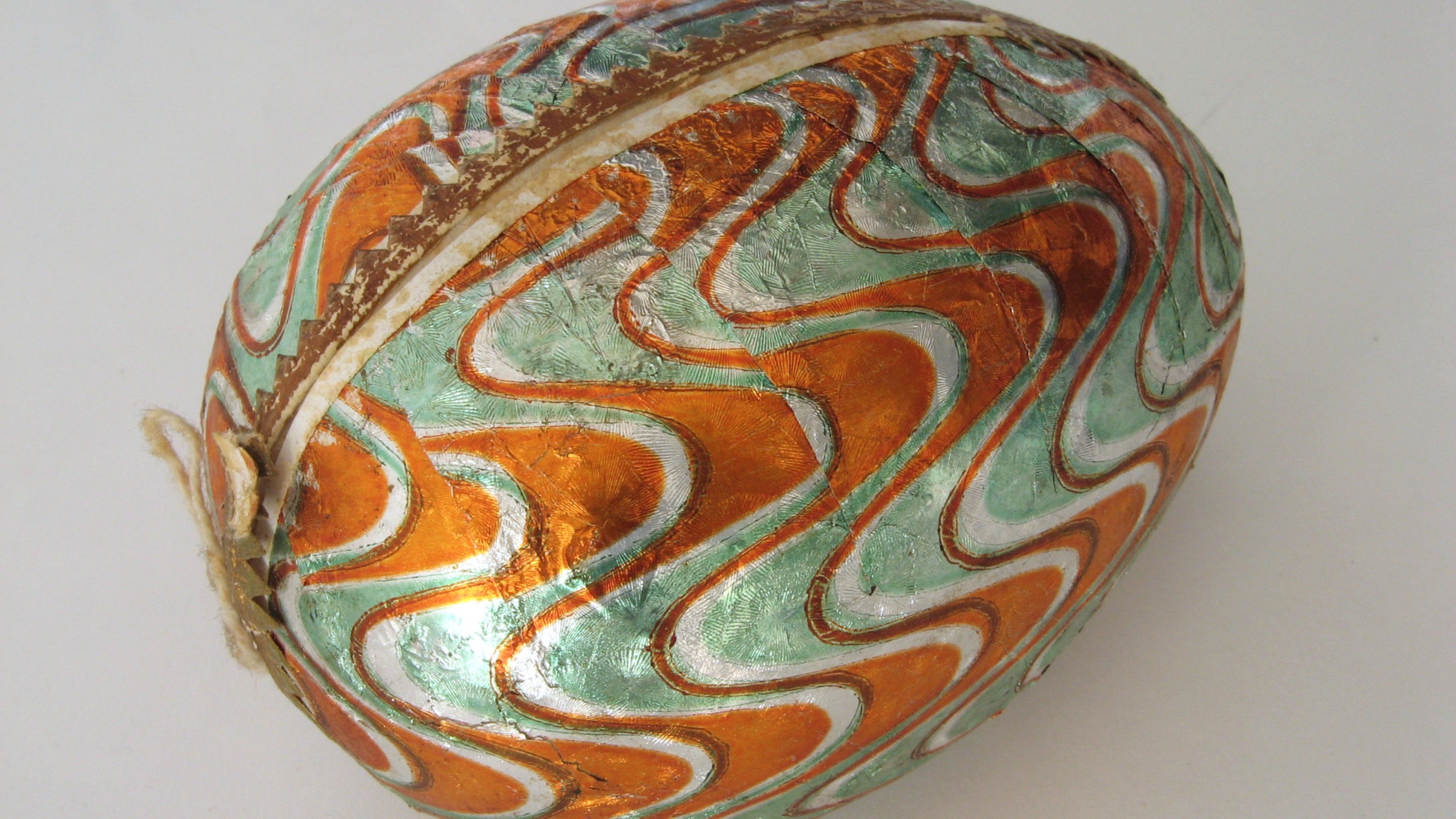 A papier-mache egg in the collection at Tyntesfield, with orange, green and white wave pattern, and a serrated gold band where the two halves are joined.