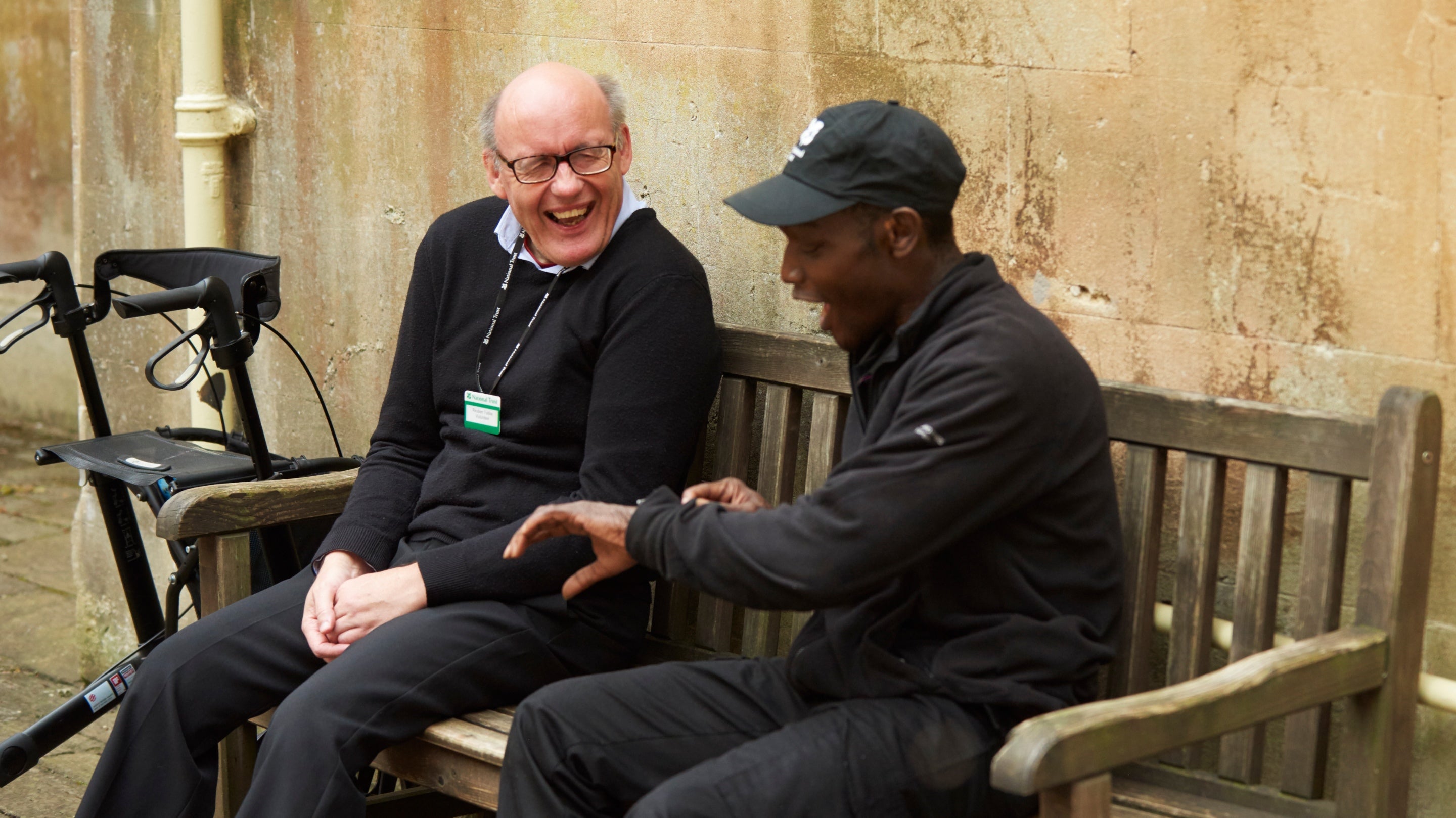 Two male volunteers sit on a bench, chatting and laughing