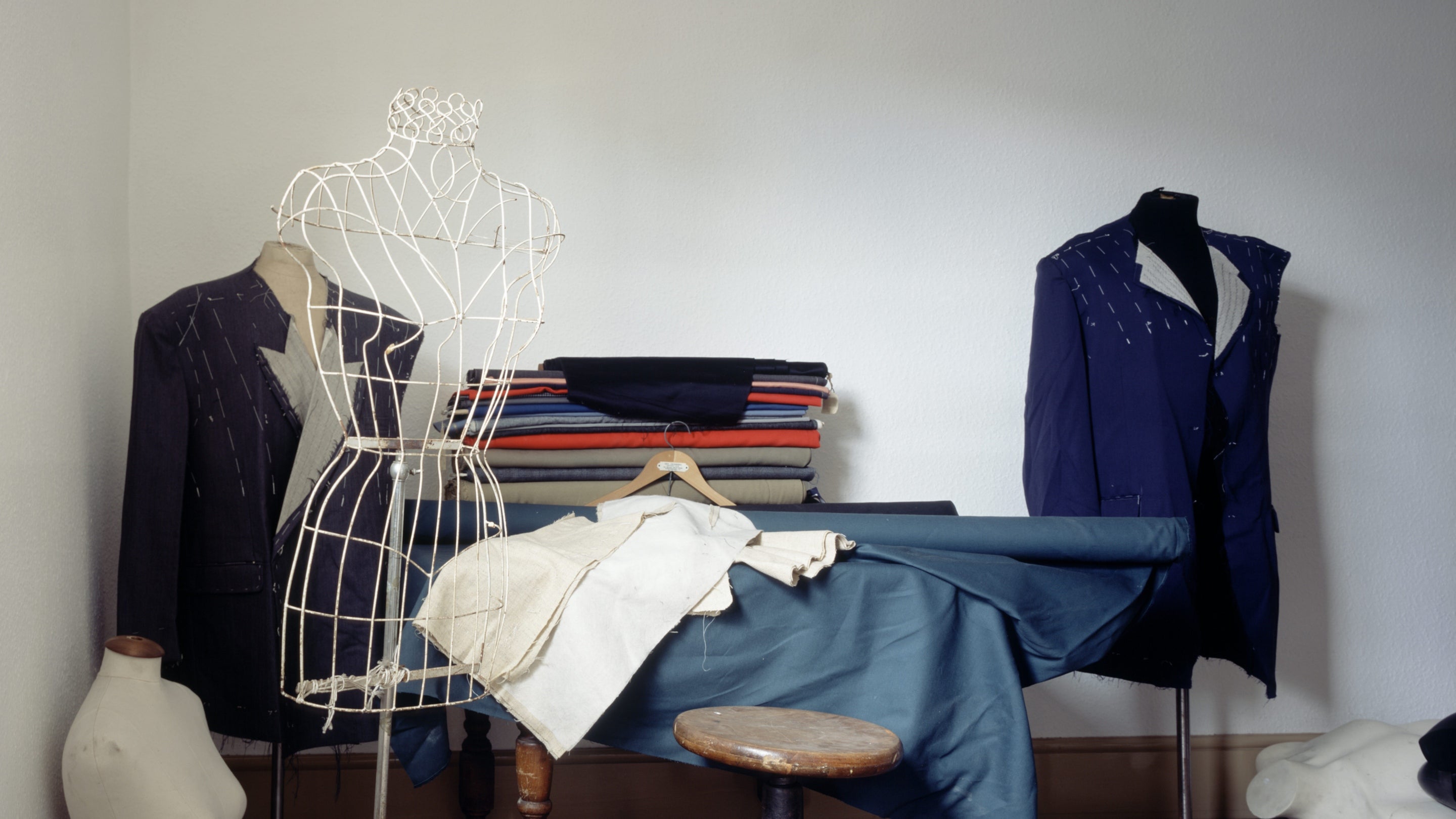 An upstairs room in the Tailor's Shop in the Birmingham Back to Backs showing dummies, rolls of cloth and unfinished suits. There is woodchip wallpaper on the walls.