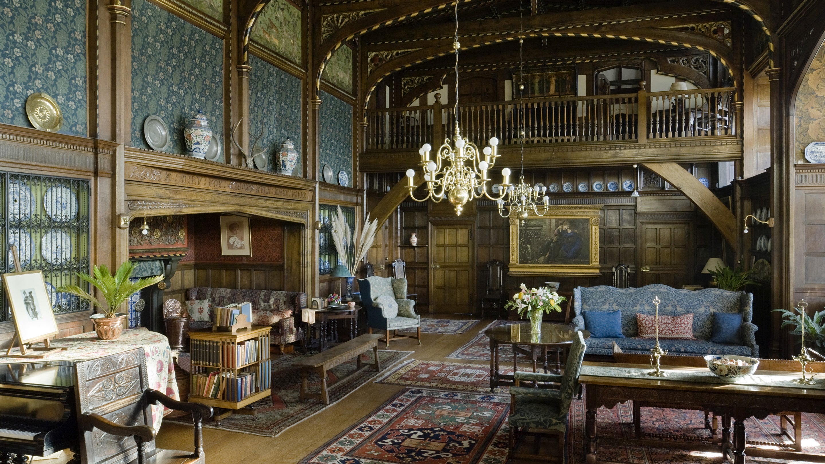 The Great Parlour, looking towards the Minstrels' Gallery, at Wightwick Manor, gives the impression of a fifteenth-century great hall converted to a late Victorian living room. The panelling is oak, some of it Jacobean, and the roof timbers and fireplace are richly carved and picked out in red, green, gold and black.