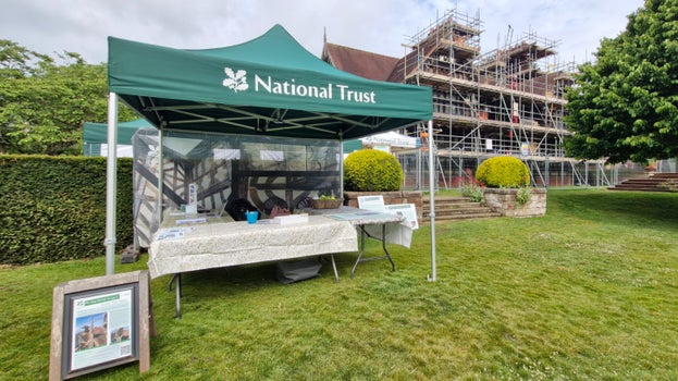 A National Trust gazebo is erected in front of the scaffolded east wing of Wightwick Manor during Phase 3 of the Big MEND project. There is information displayed about the conservation project and large images of the details of the woodwork on the Manor are on a banner hanging inside.