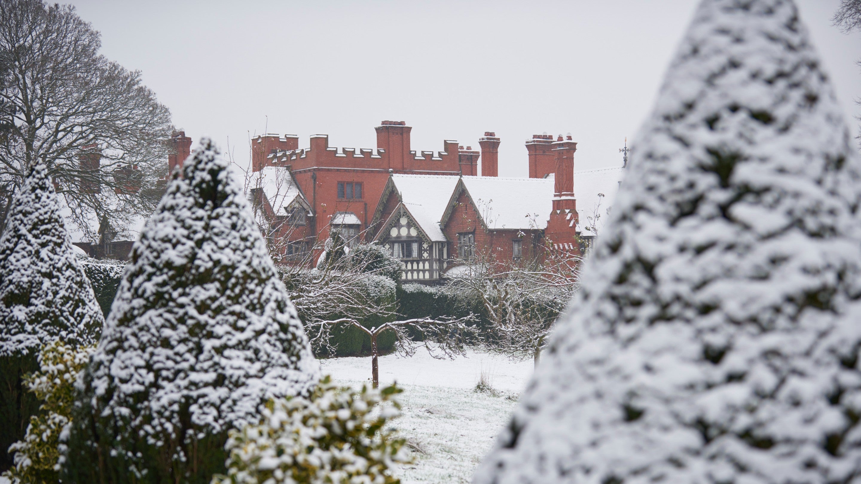A view towards Wightwick Manor from the snowy orchard, everything is covered in snow.