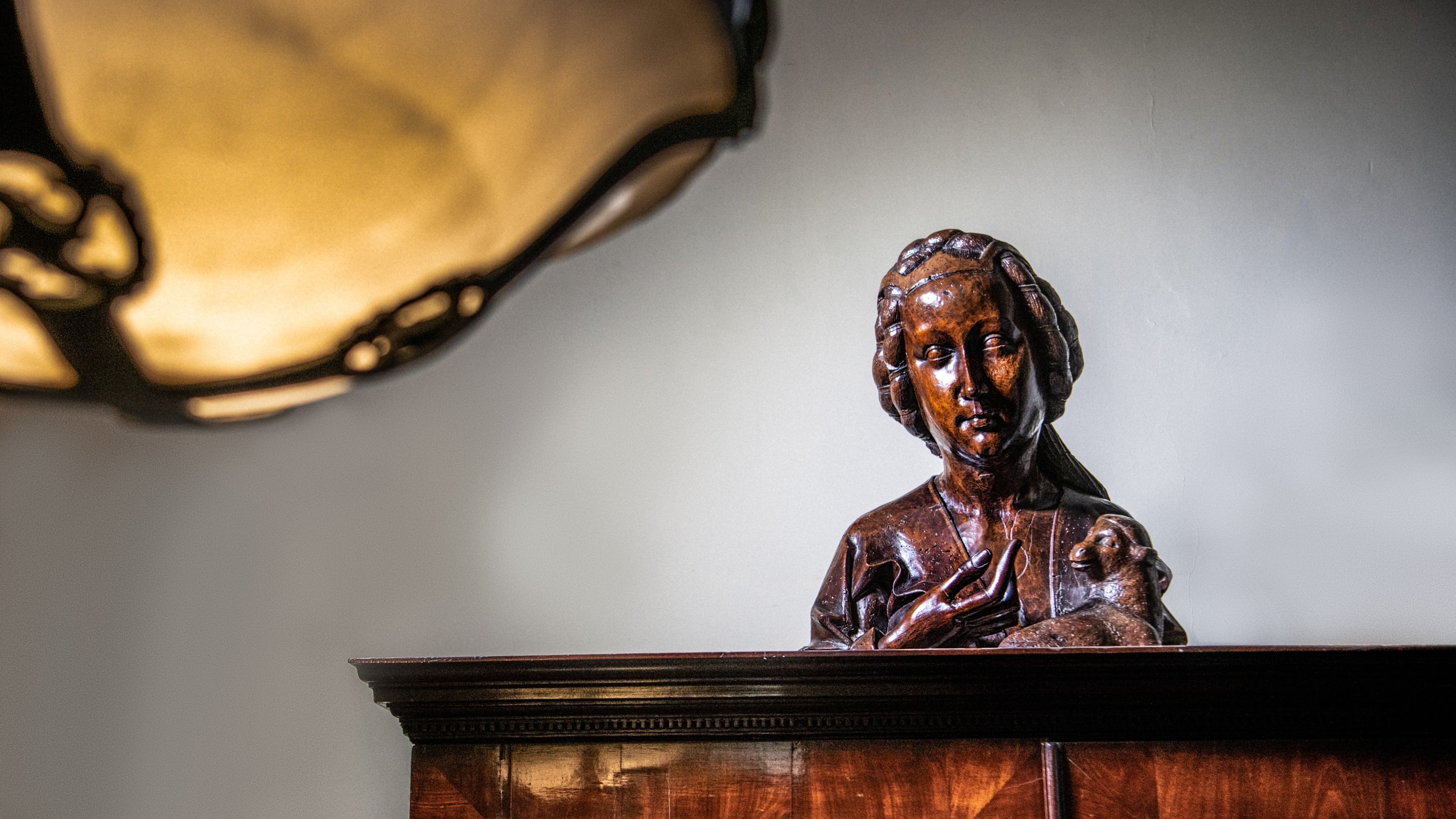 The wooden sculpture of St Agnes show sitting on top of a wooden cupboard at Anglesey Abbey in Cambridgeshire