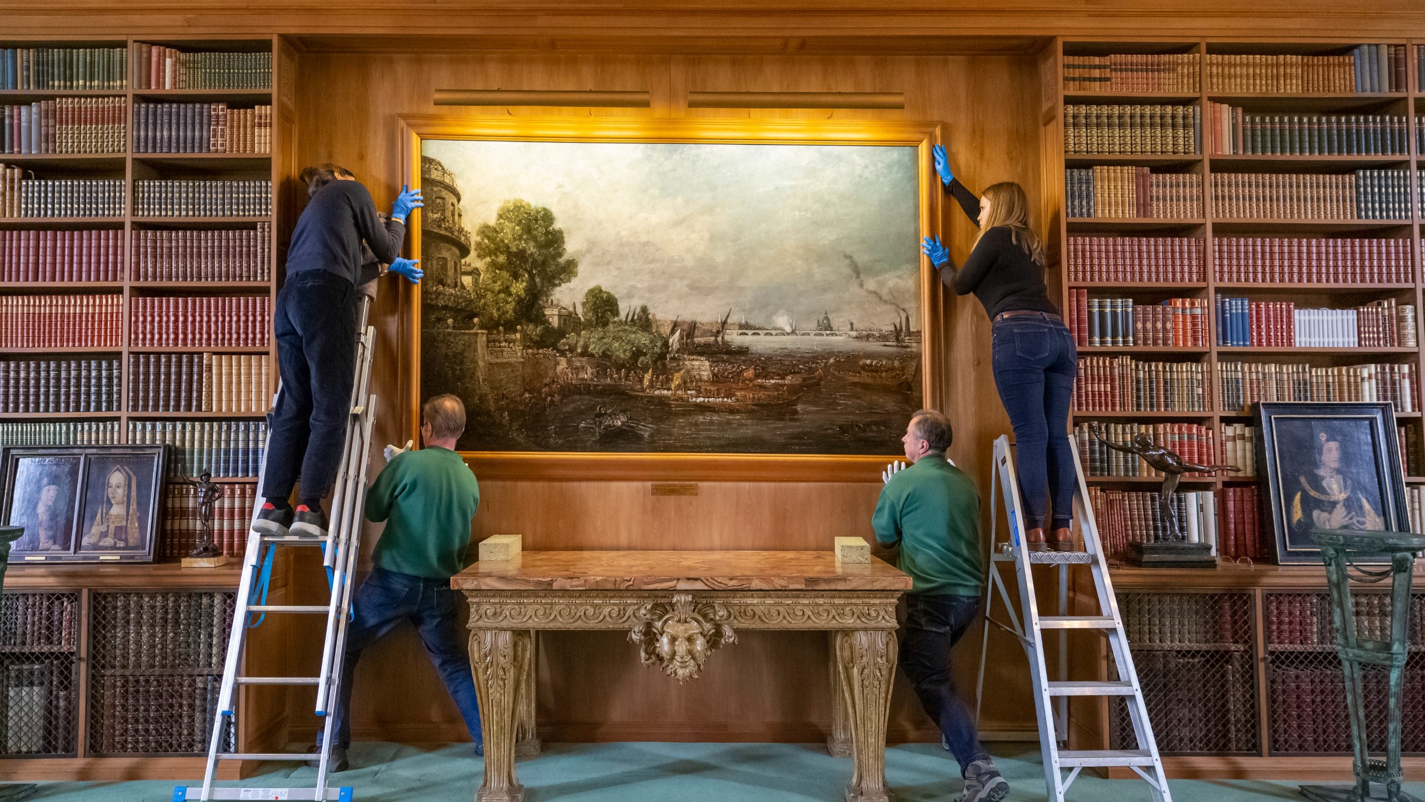 Four people re-hanging the Constable painting at Anglesey Abbey, Cambridgeshire