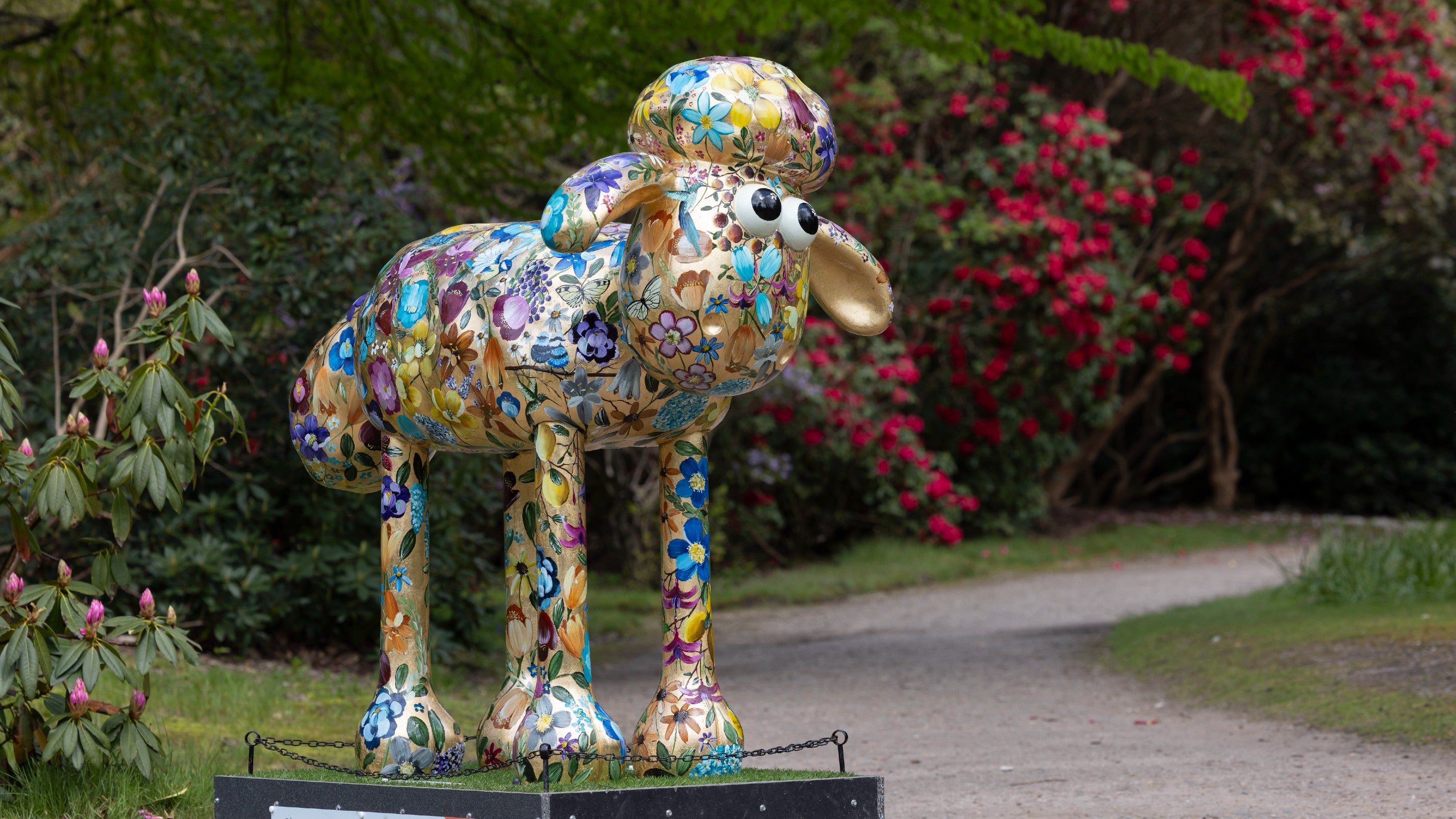 A funky golden painted Shaun the Sheep sculpture stands on a winding garden path.