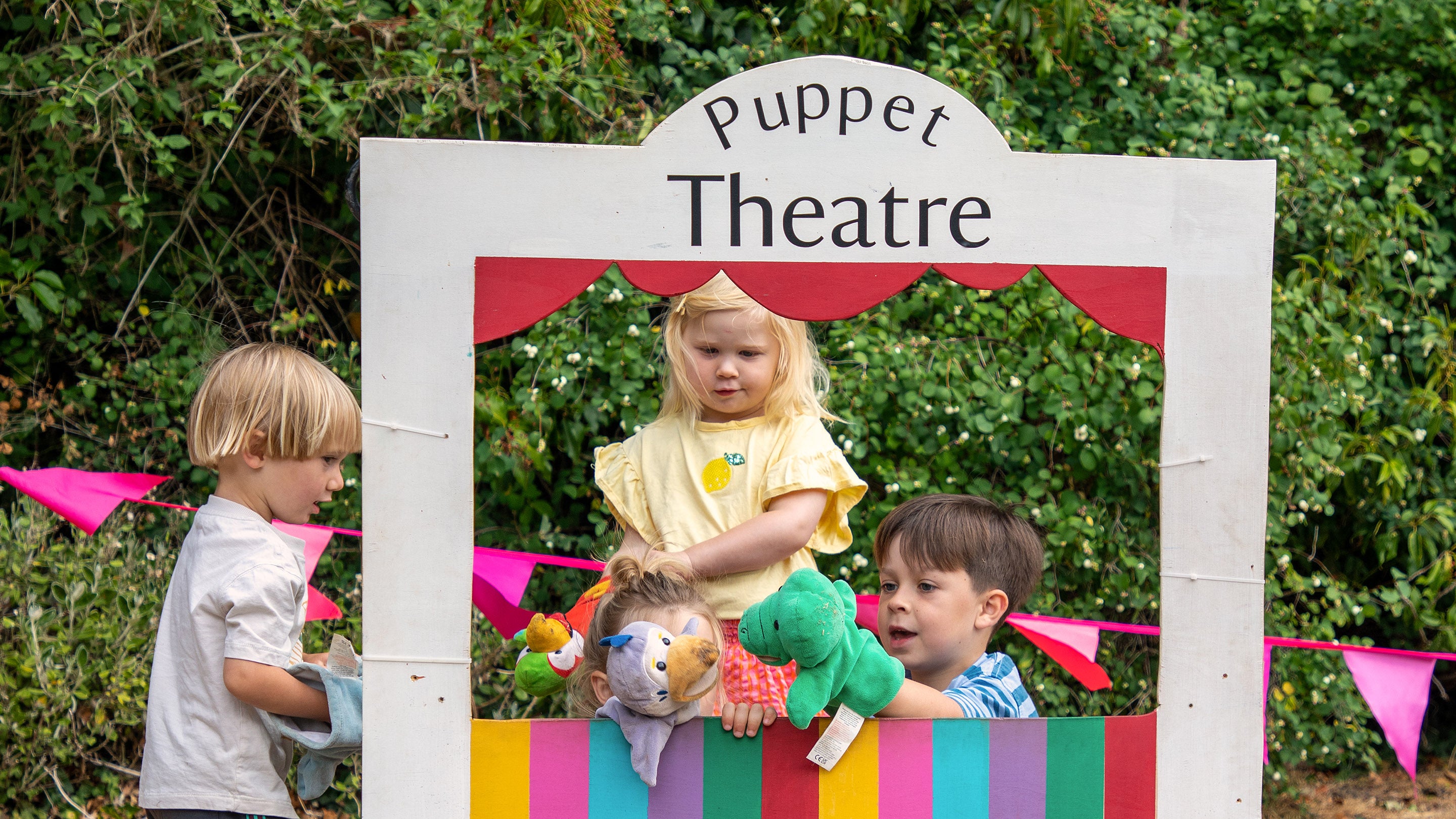 A group of young children playing in a puppet theatre. They have animal glove puppets and are performing a show.