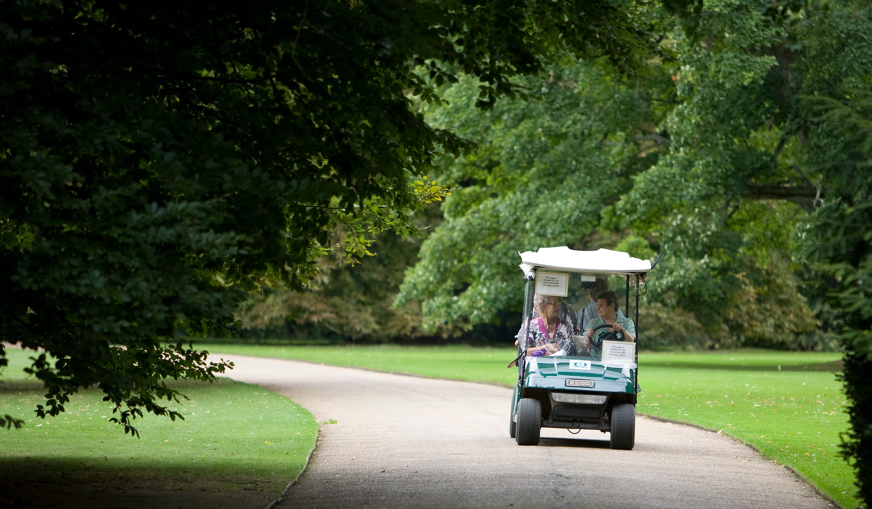 A golf cart style buggy being driven along a driveway in a historic parkland