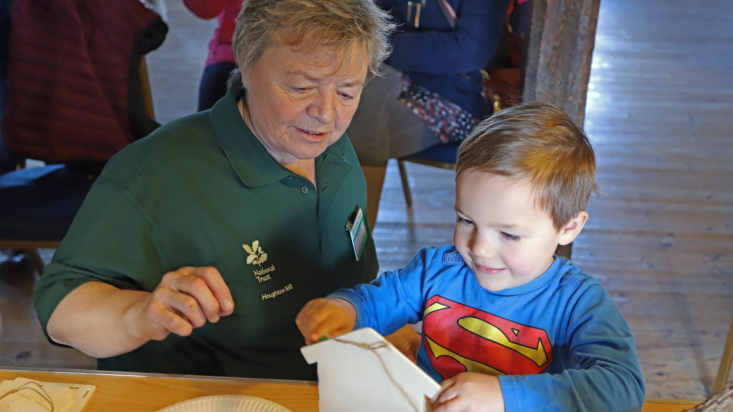 A volunteer helping a child to make bird-feeding trays during a campsite open day at Houghton Mill and Waterclose Meadows, Cambridgeshire.