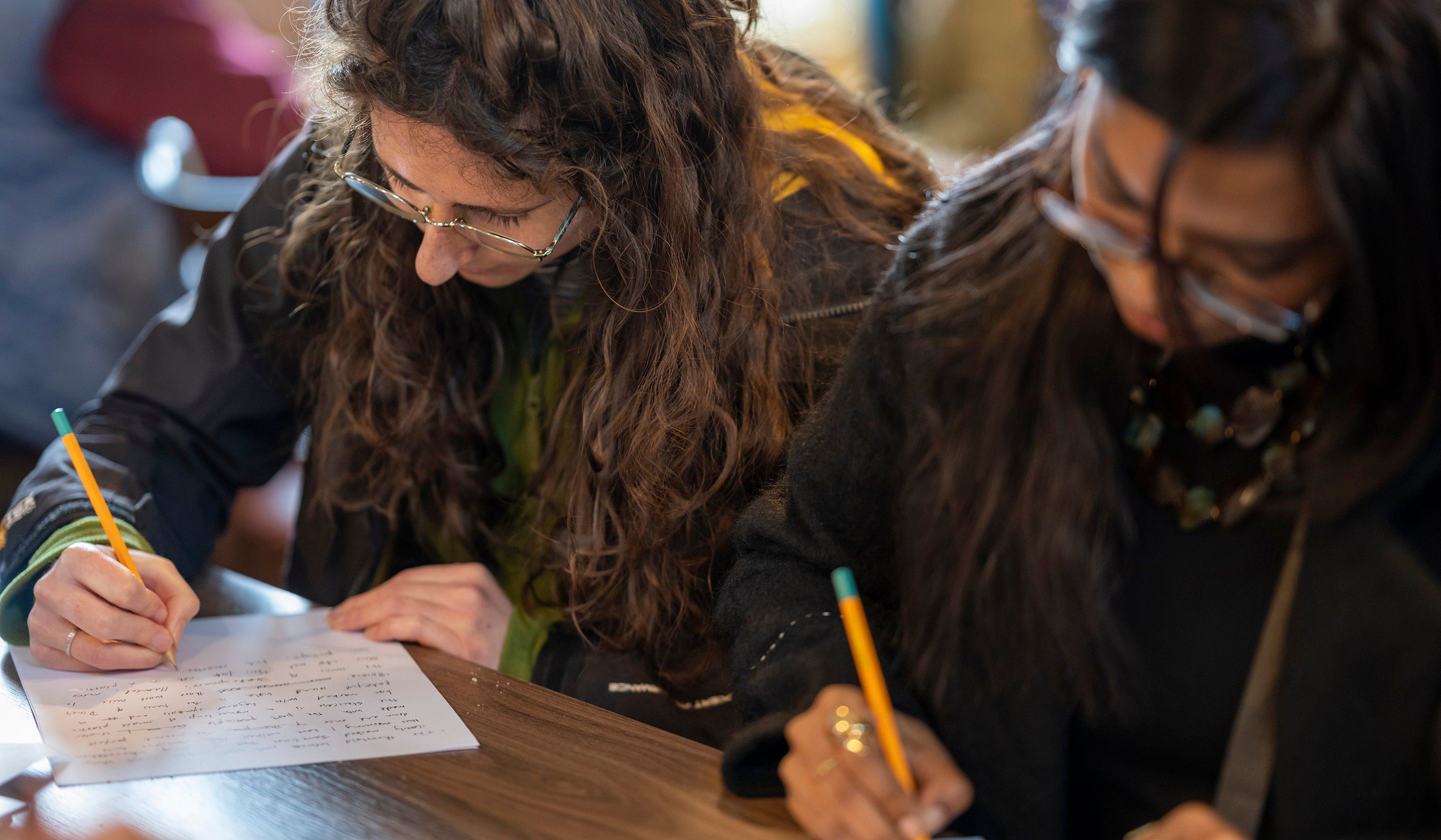 Two young women concentrating hard while writing in a workshop