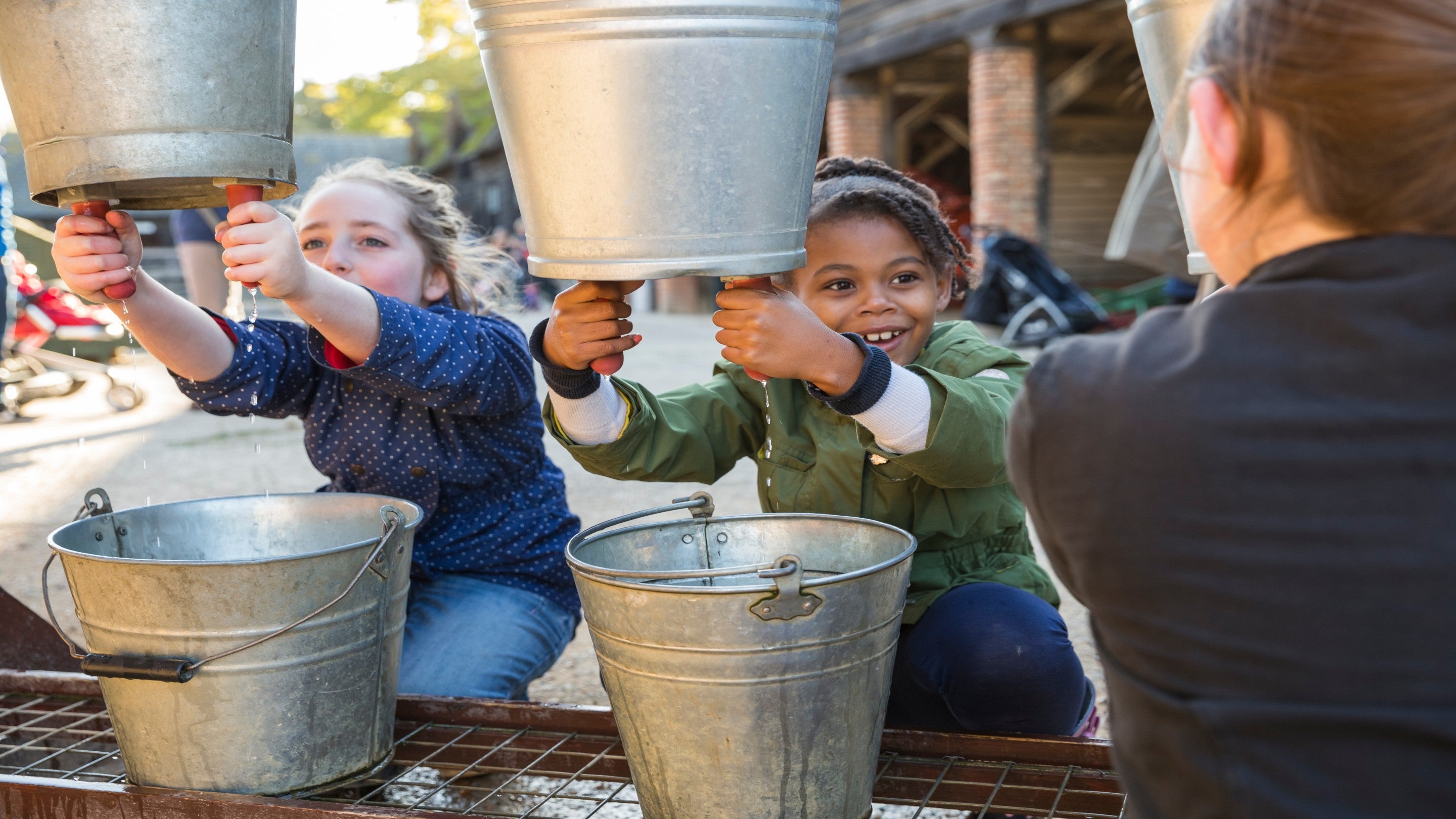 Children smile at each other as they try out a milking machine activity at Wimpole Estate during Harv'Fest event