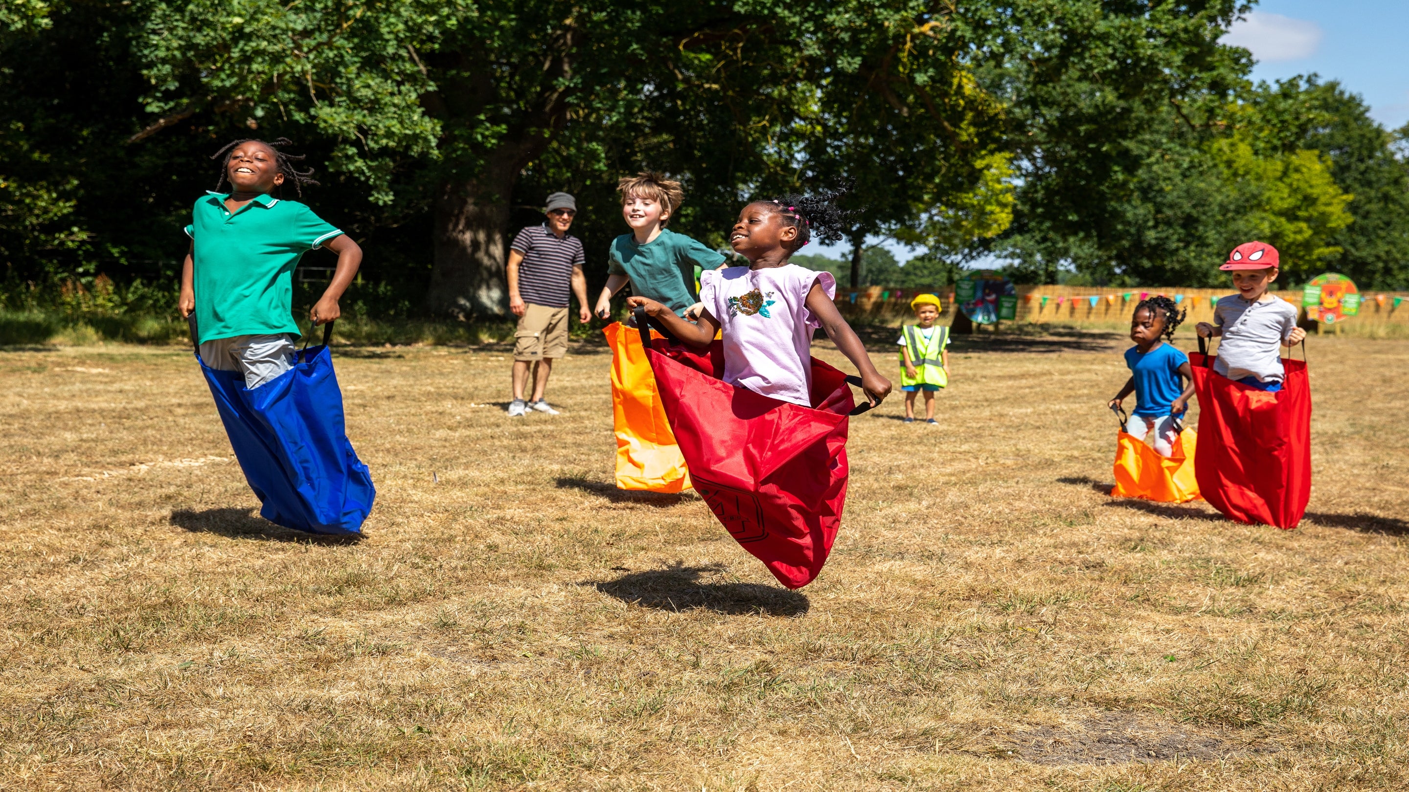 5 children of mixed ages enjoy a sack race on the Wimpole Estate Summer of Play field
