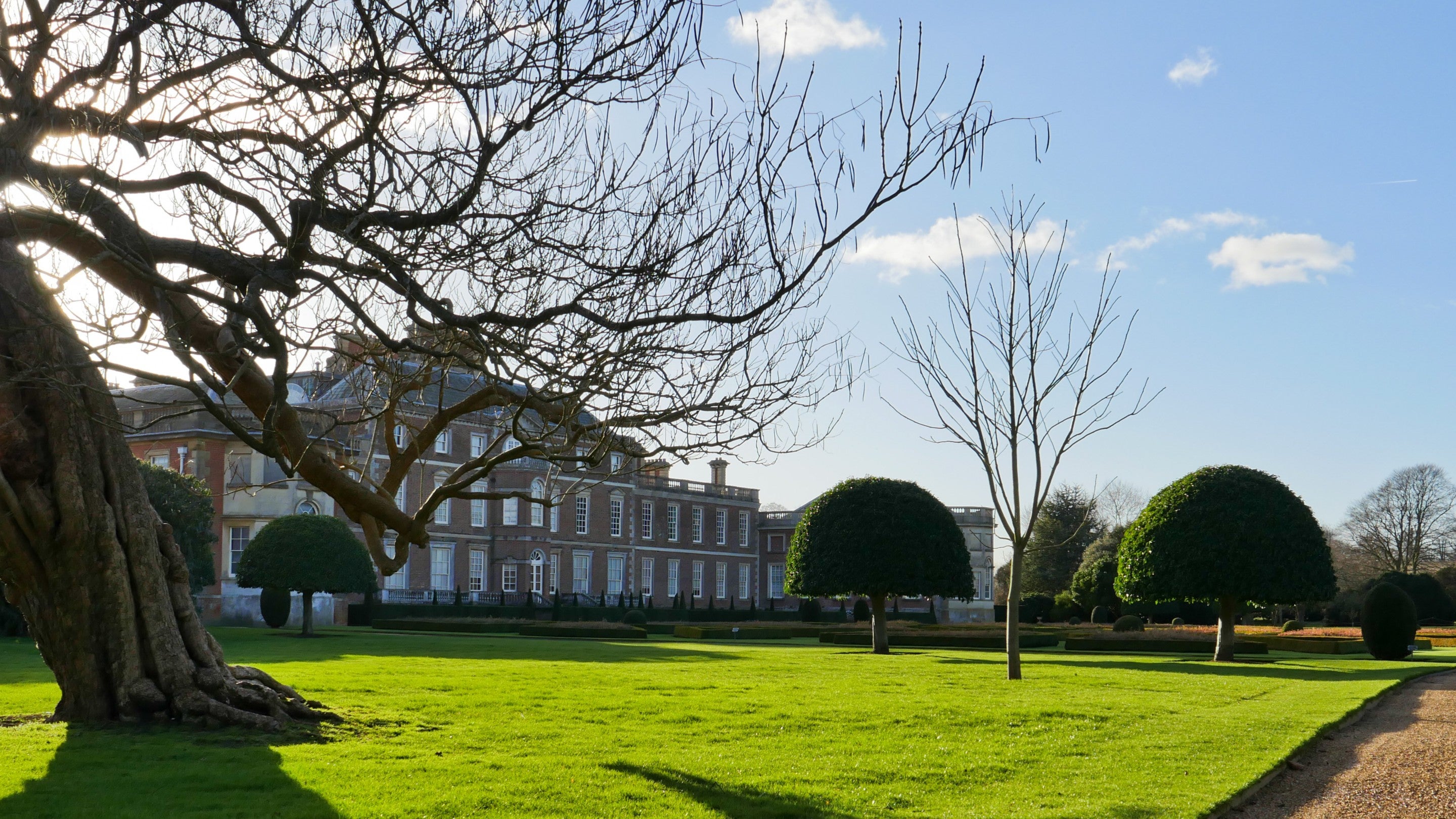 A winter scene showing the exterior of Wimpole Hall, with bright blue skies and bare trees.