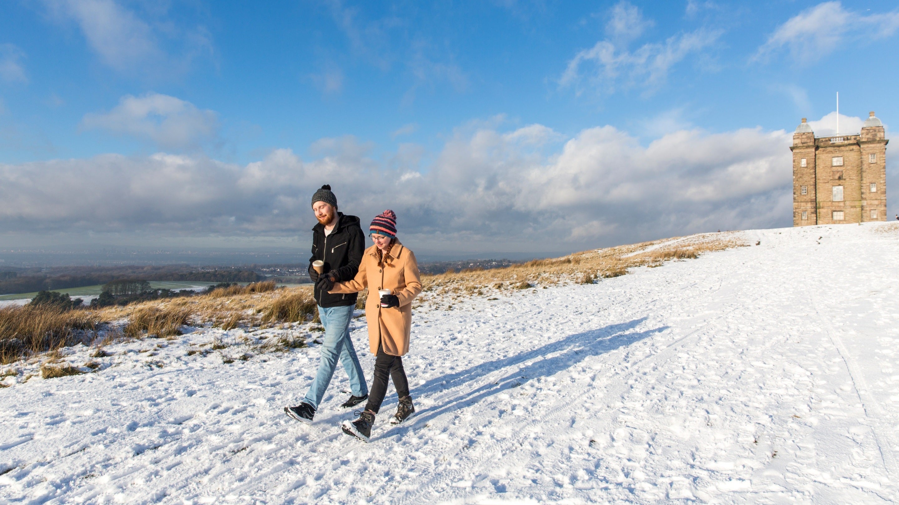 Visitors wearing woolly hats walking in the snow. in front of the Cage at Lyme, Cheshire