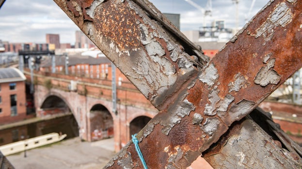 Close up detail of two metal trusses on Castlefield Viaduct. The city skyline can be seen in the background.