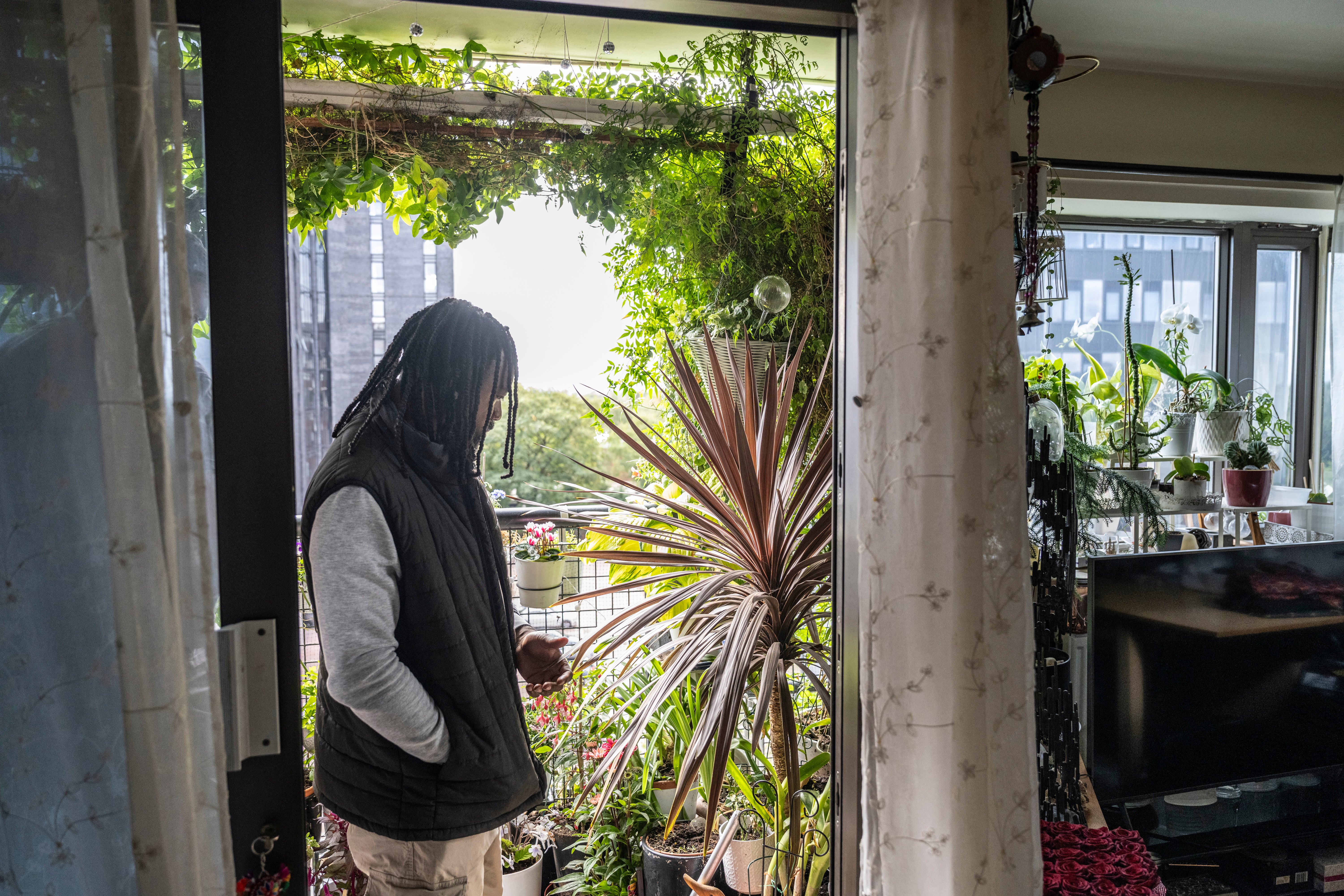 One of the judges of the National Trust's Sky Gardening Challenge 2025 stands in the doorway to a balcony which is covered in lush green plants. Beyond is a view of the Manchester skyline.