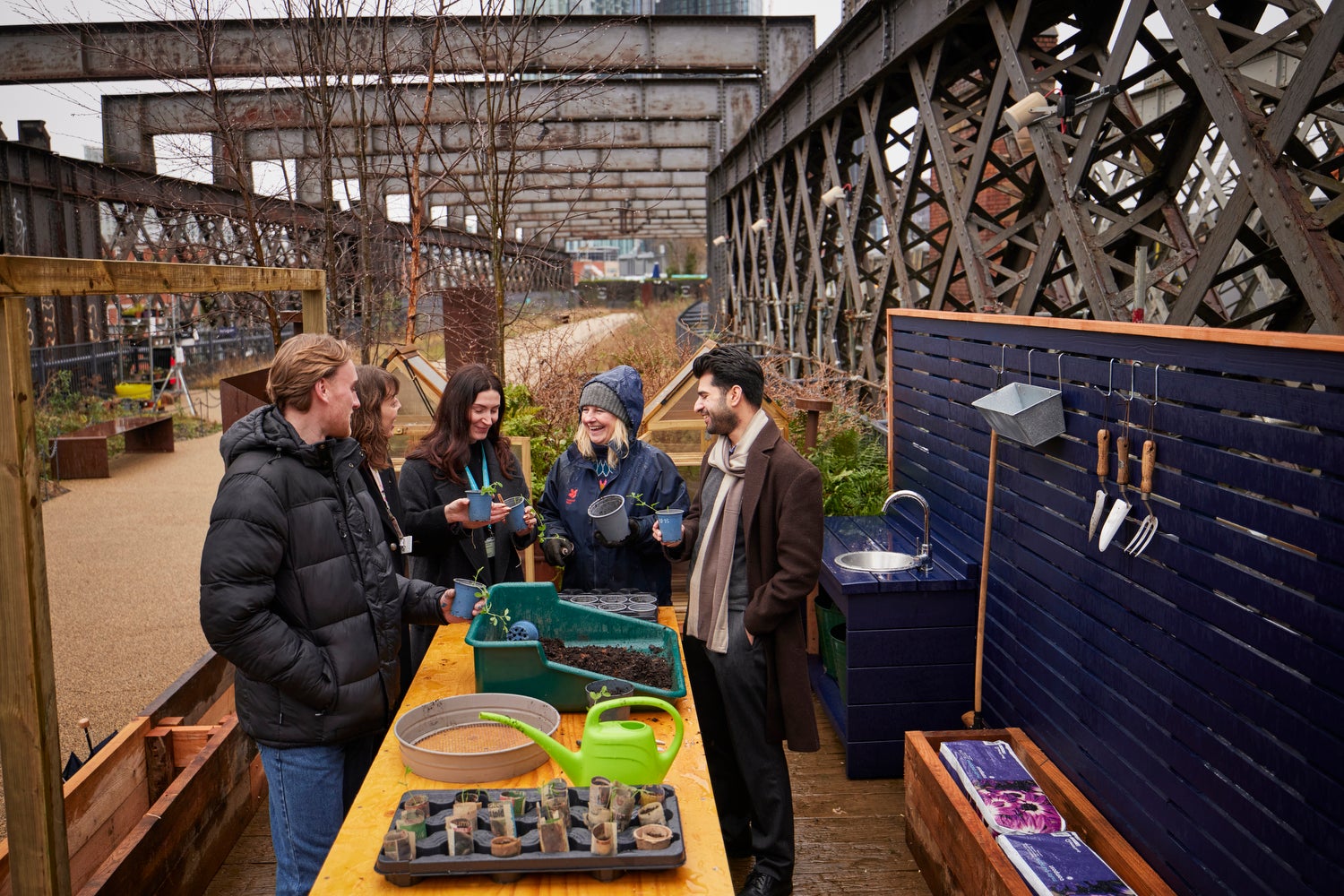 A group of people outside stood around a large work bench each holding a flower pot