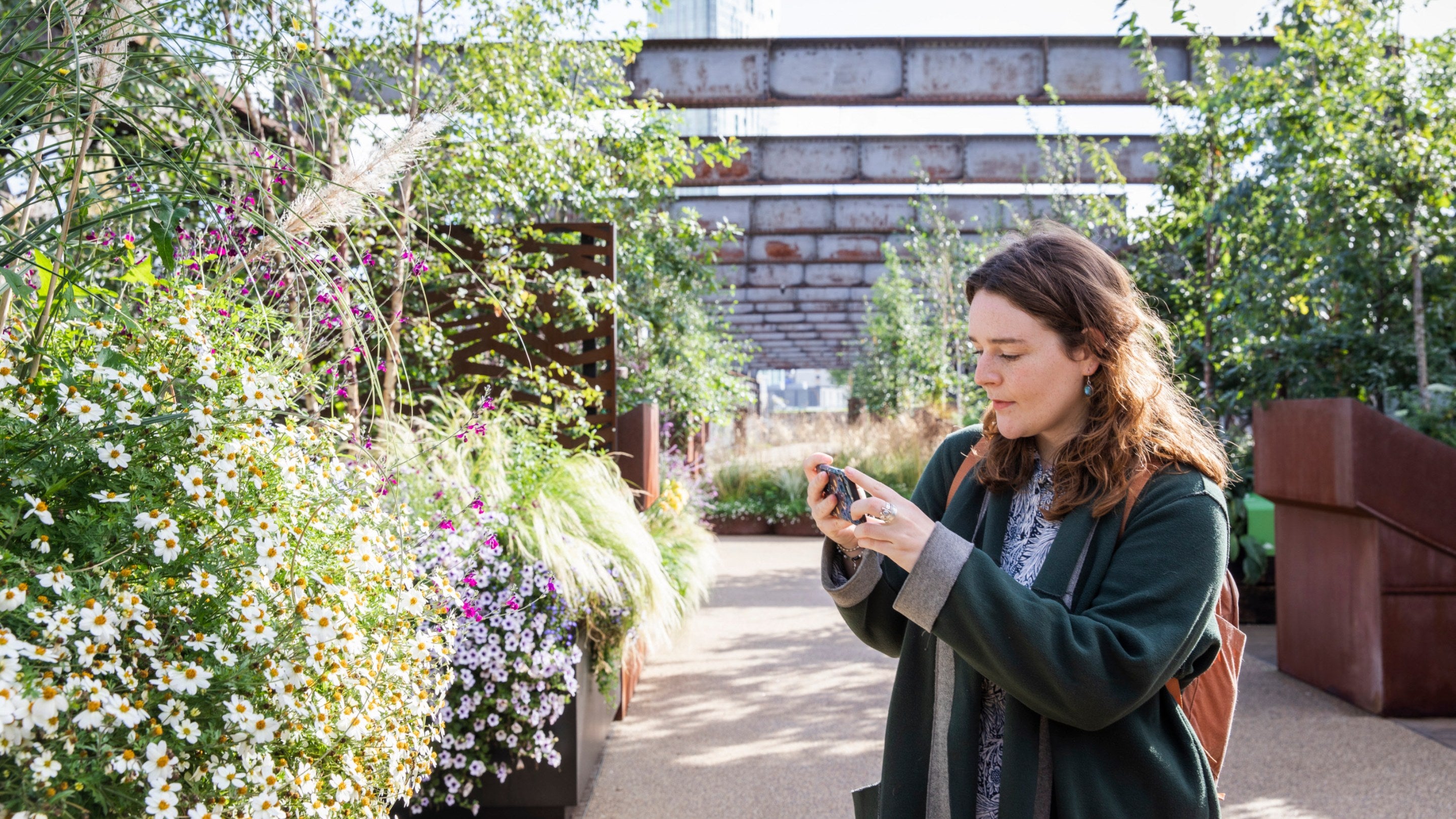 A visitor exploring and taking a picture in the urban garden at Castlefield Viaduct, Manchester