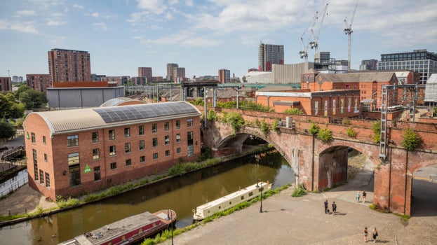 A view looking over the city and canal from Castlefield Viaduct, with features such as the large brick-built bridge, buildings and skyscrapers visible beyond the canal.
