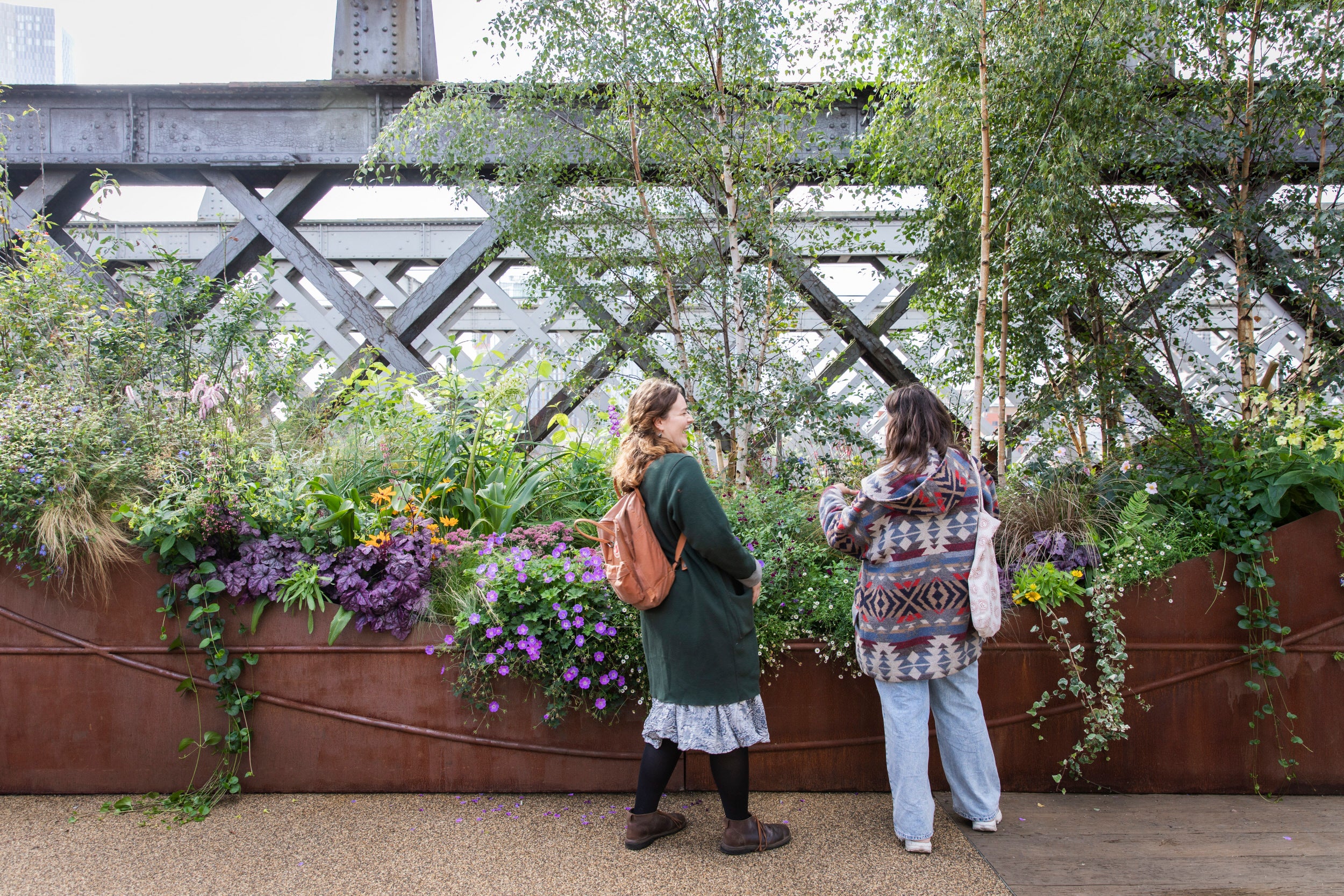 Two young women in winter coats standing by a planter filled with plants and trees