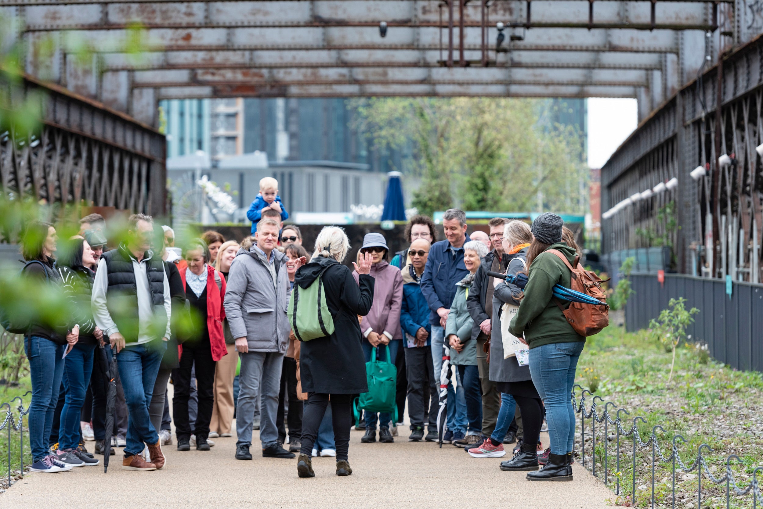A group of people of various ages being talked to by a guide and surrounded by the old steel girders of a railway viaduct.