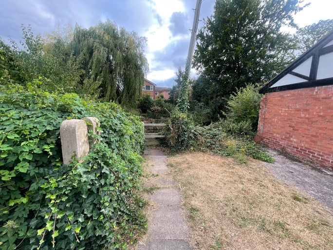 A thin track with a wall covered in ivy to the right and a building to the right.
