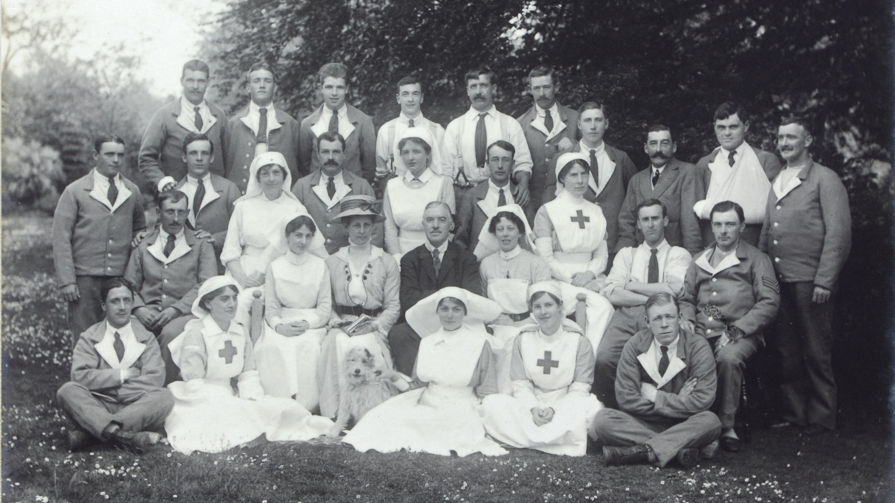 A black-and-white photograph showing a group of nurses and soldiers posed in a woodland.
