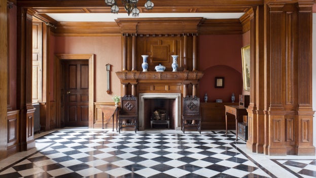 A spacious room featuring a black and white checkered floor with wooden panelling and large fireplace in the middle.