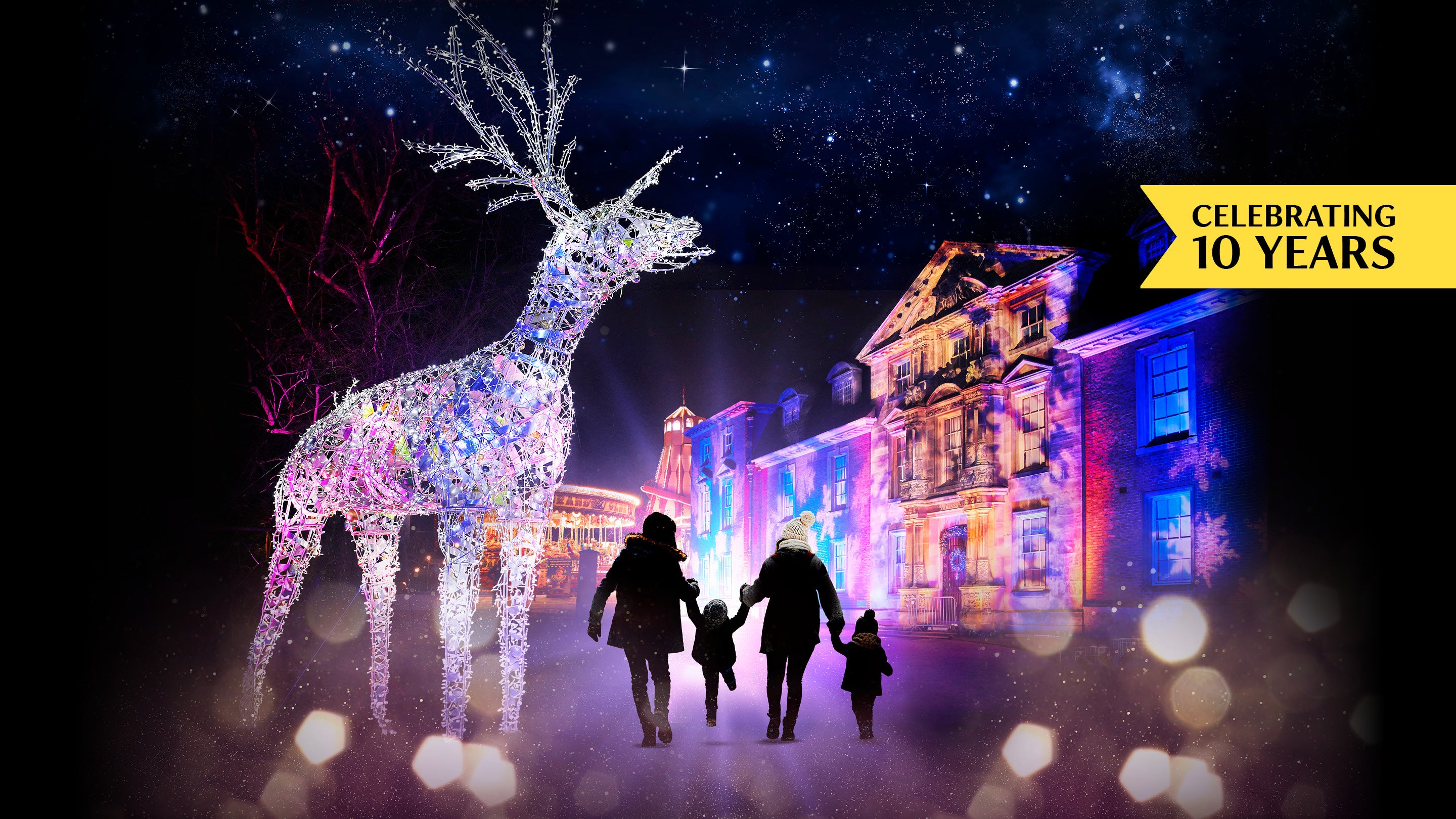 A large illuminated reindeer statue stands in front of a historic building, adorned with Christmas lights at Dunham Massey. A family is seen walking towards the building.