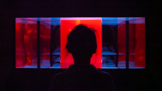 A person stands in front of a vibrant red and blue illuminated display, creating a striking visual contrast.