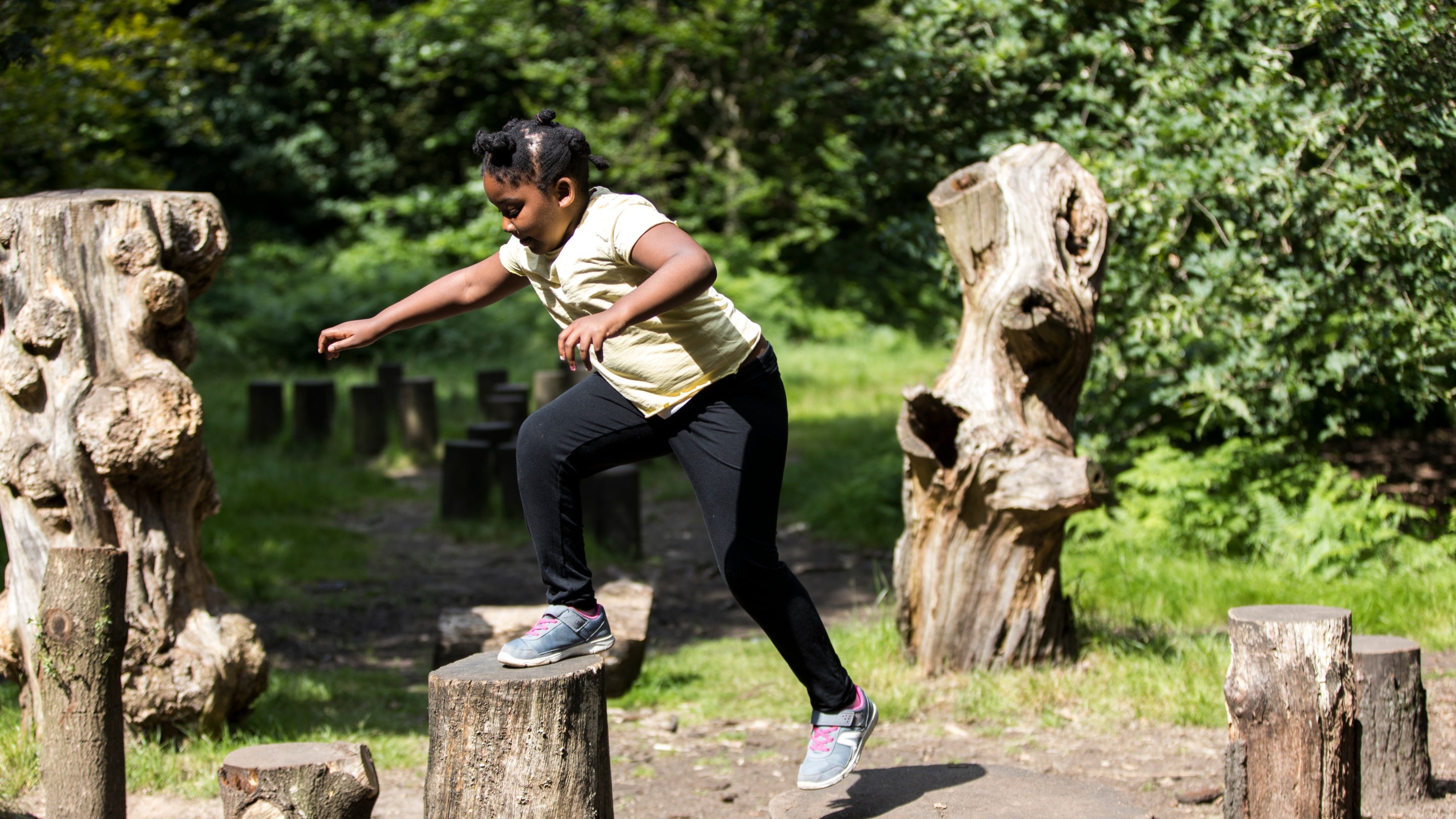 A teenage girl jumping from one log to another in the natural play area at Dunham Massey, Cheshire.
