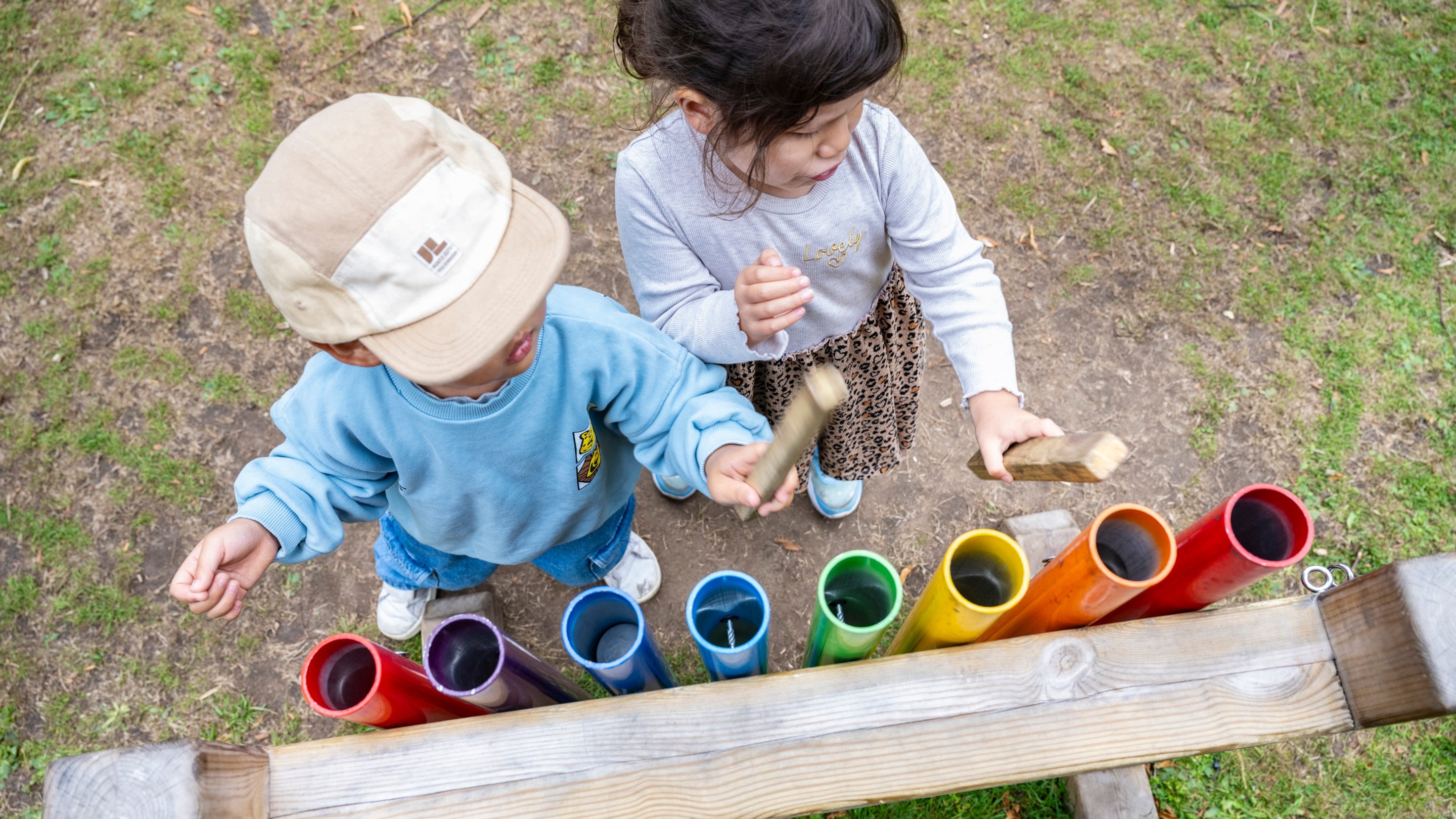 Two children engaged in play with vibrant wooden blocks beside a large musical instrument during the Summer of Play.