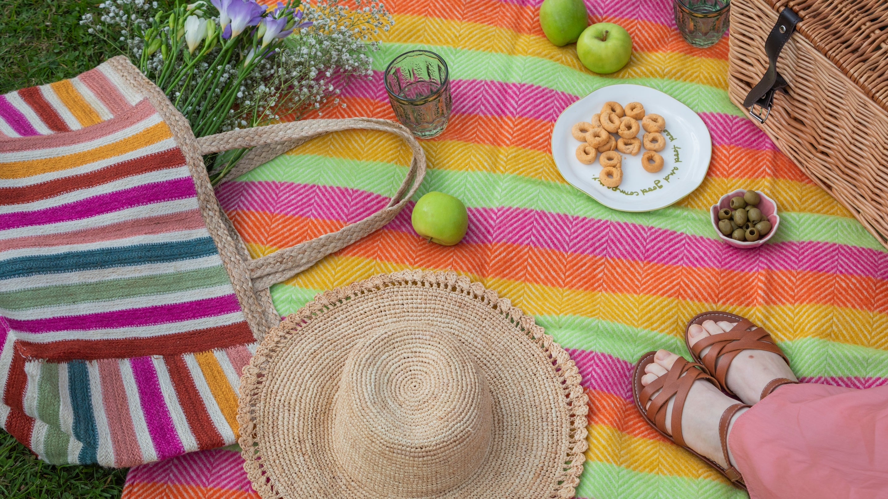A picnic scene with a blanket, a basket filled with food, and a pair of shoes resting beside it.