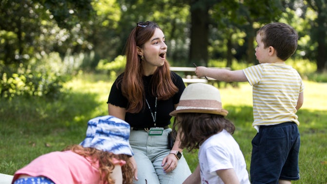 A member of staff engaging three children with nature activities in a woodland at Dunham Massey