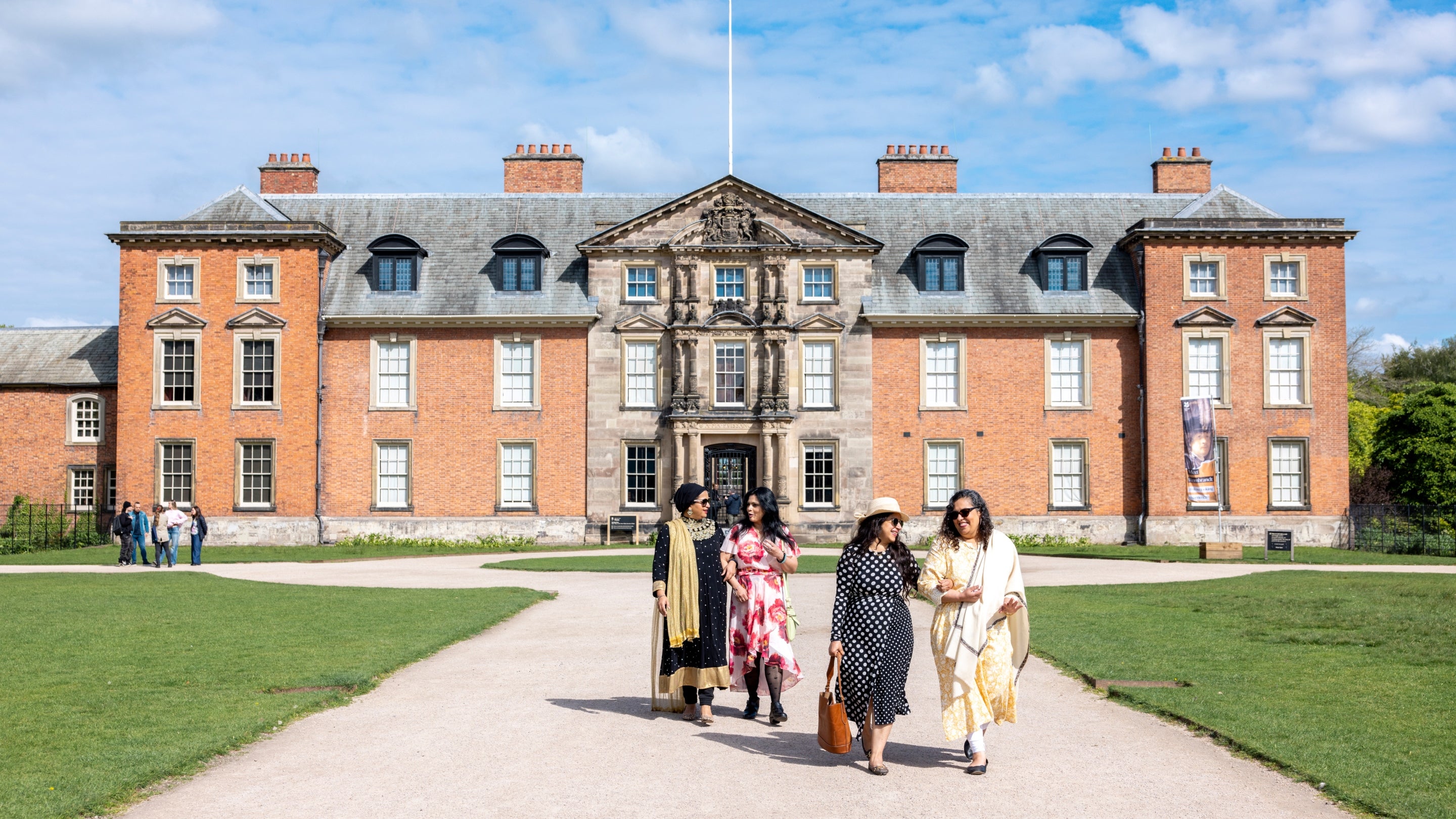 A group of visitors walking around Dunham Massey house on a sunny day.