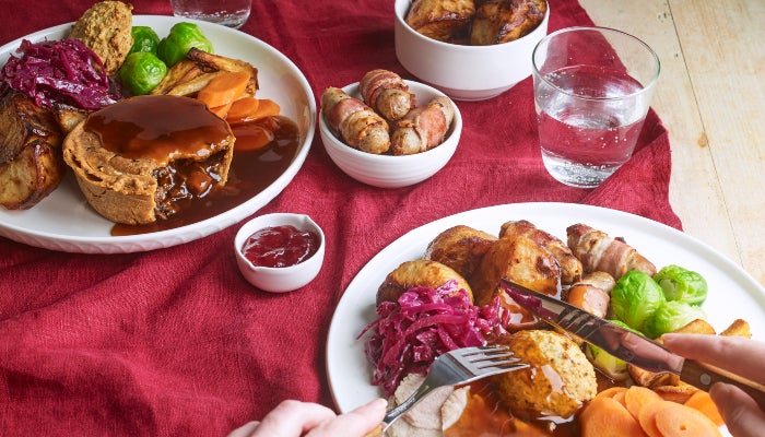 A person tucks into a Christmas lunch filled with turkey, roast potatoes and all the trimmings. On the table is a vegan pie dinner, and a side of pigs in blankets.