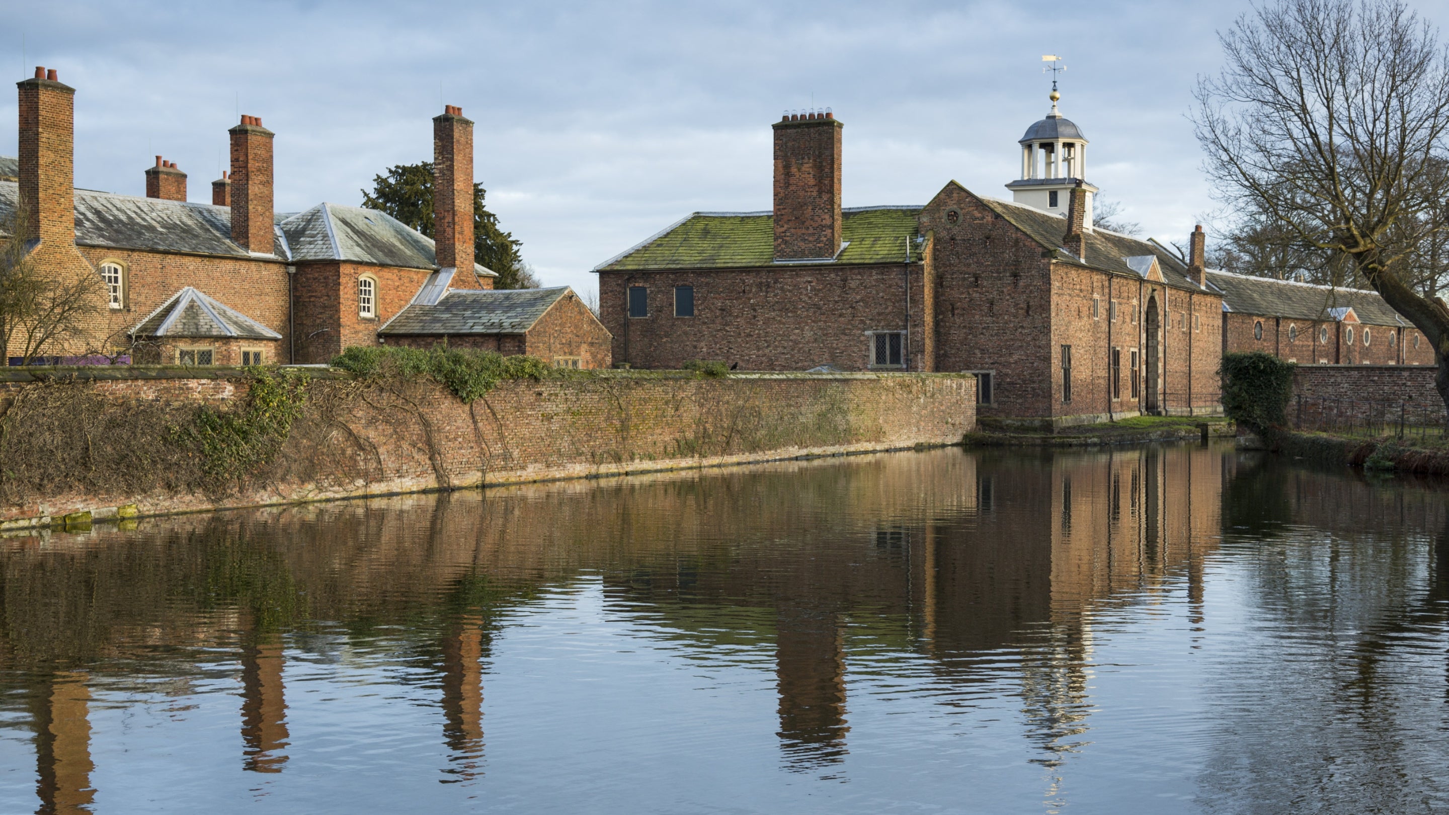 A view of the moat with Dunham Massey house, coach-house, and stables reflected in the water, Cheshire.