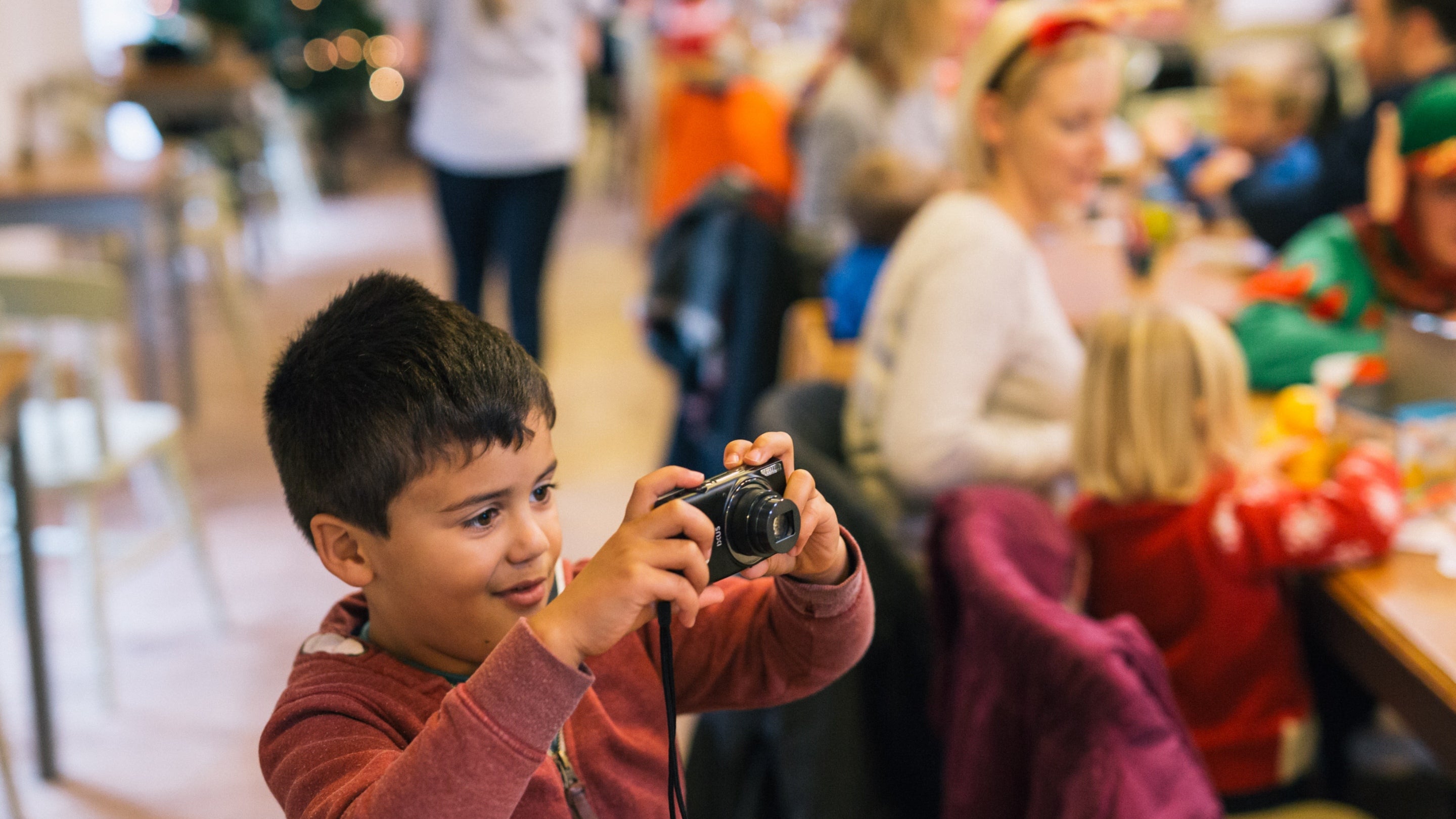 A young boy smiles while taking a photo with a camera, capturing a Christmas moment in a dining area.