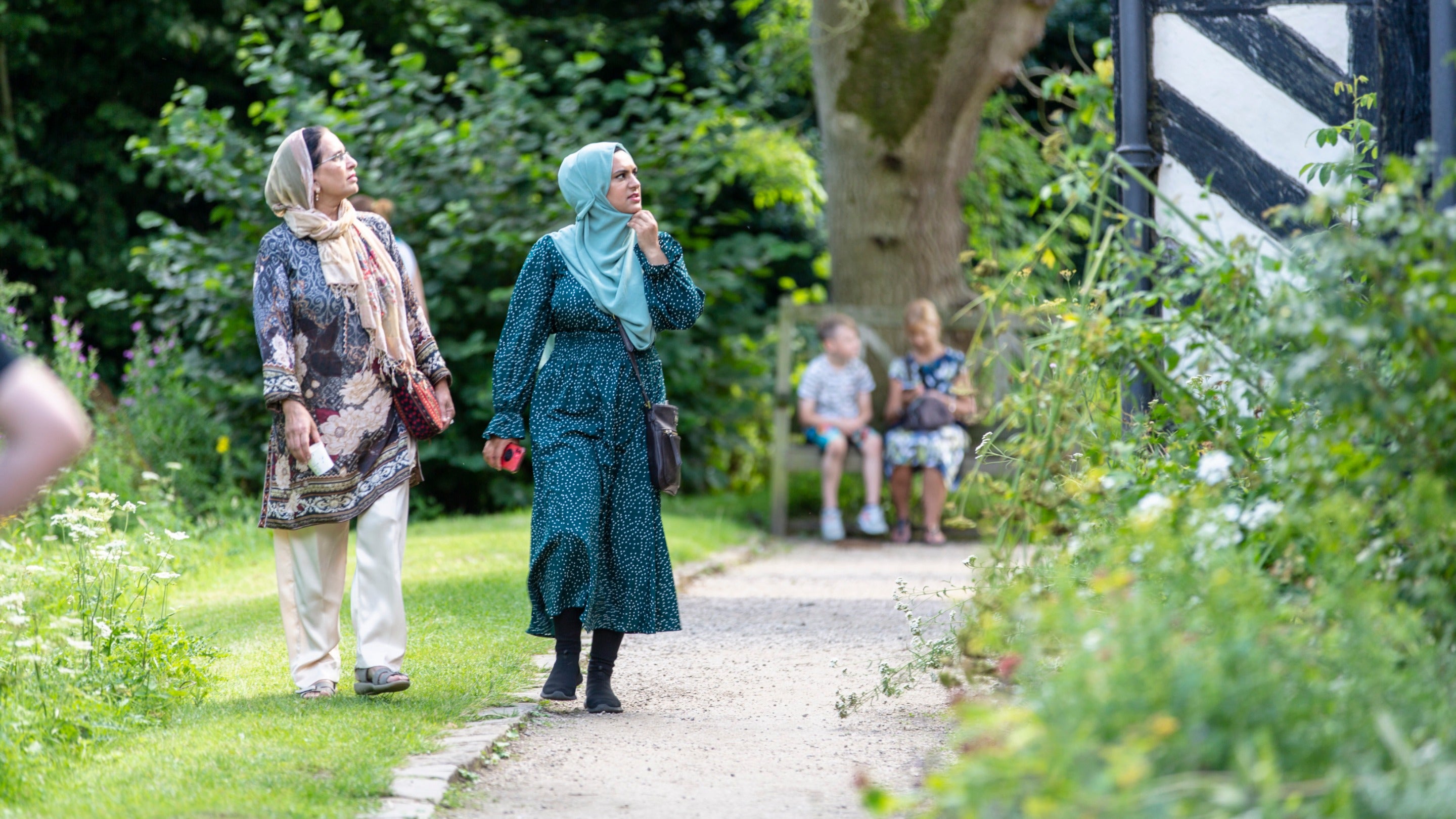 Visitors enjoying the gardens in August at Little Moreton Hall Cheshire with visitors sat on a bench near a tree in the background