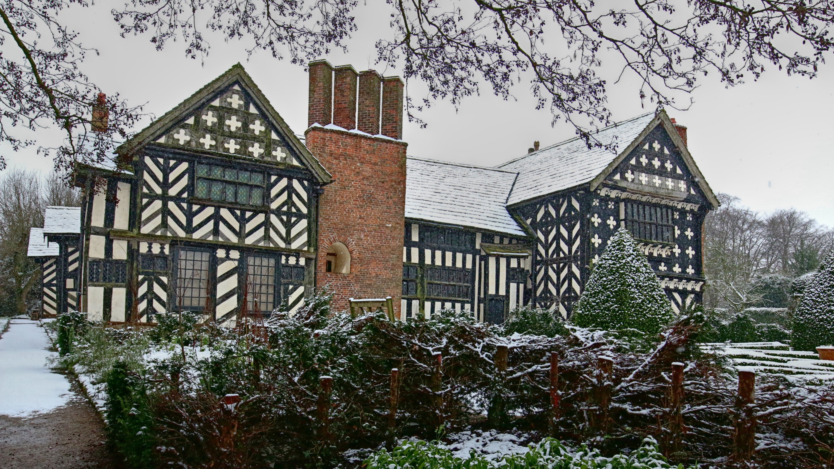 A photograph of the outside of timber-framed Little Moreton Hall, covered in snow in winter.