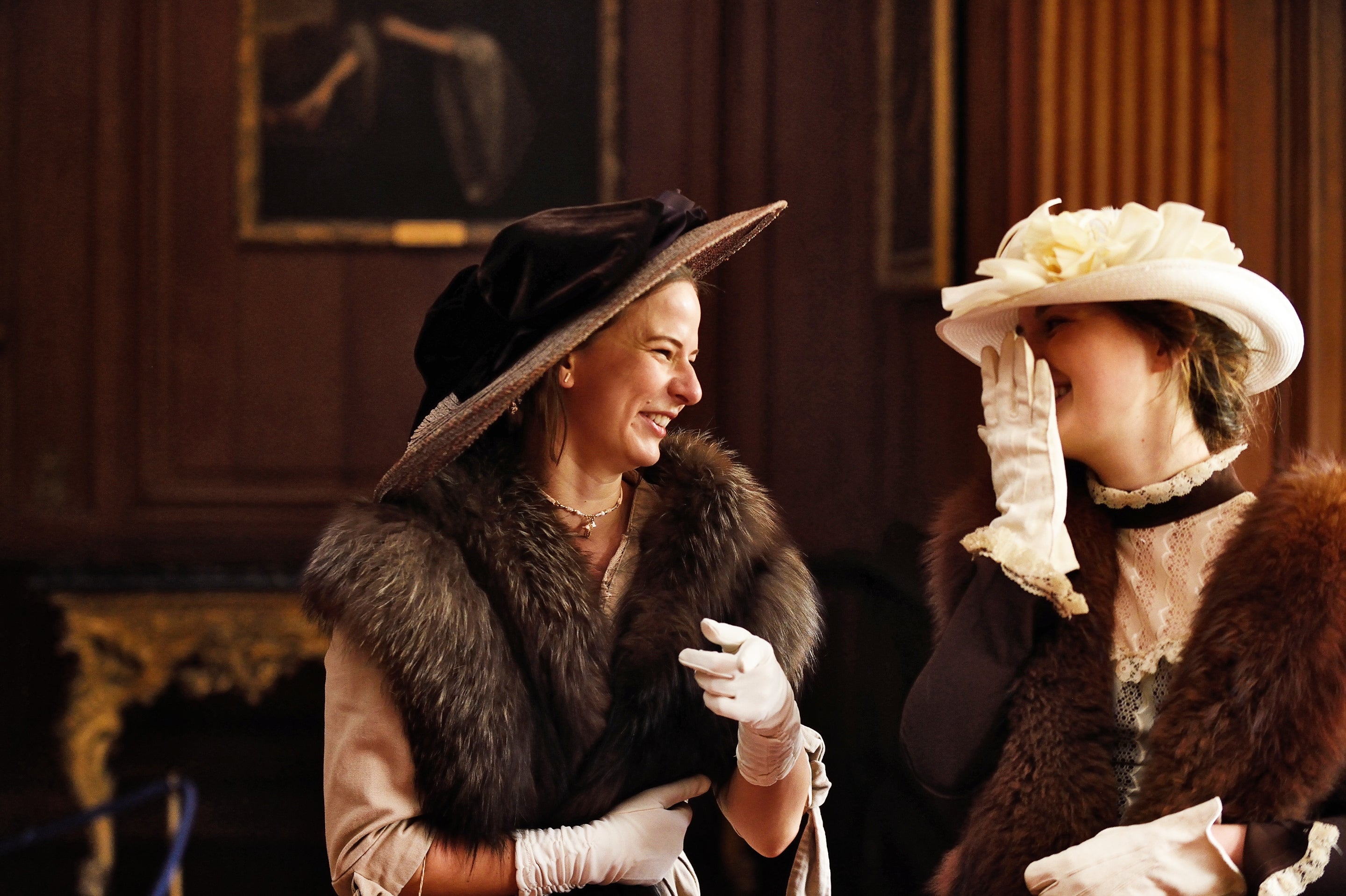 Two women wearing Regency clothes look at each other and laugh whilst exploring the house at Lyme, Cheshire.