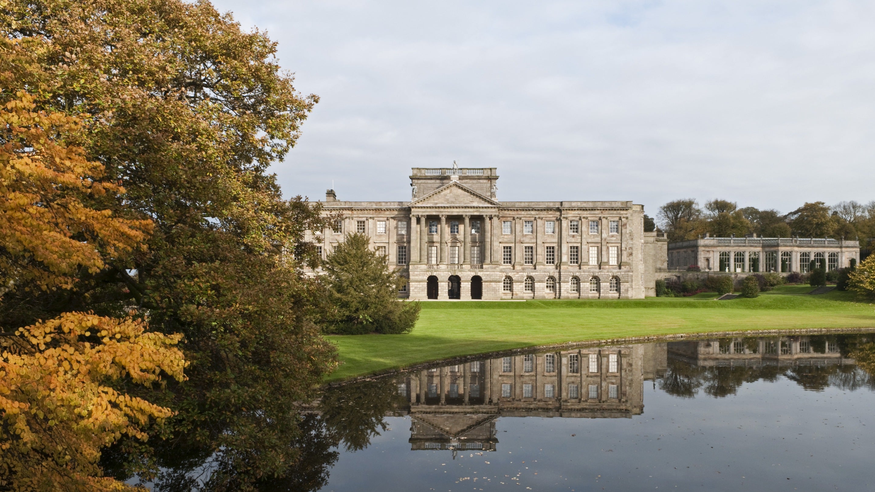 Grand house with columns reflected in a lake and surrounded with autumn trees at Lyme Park, Cheshire